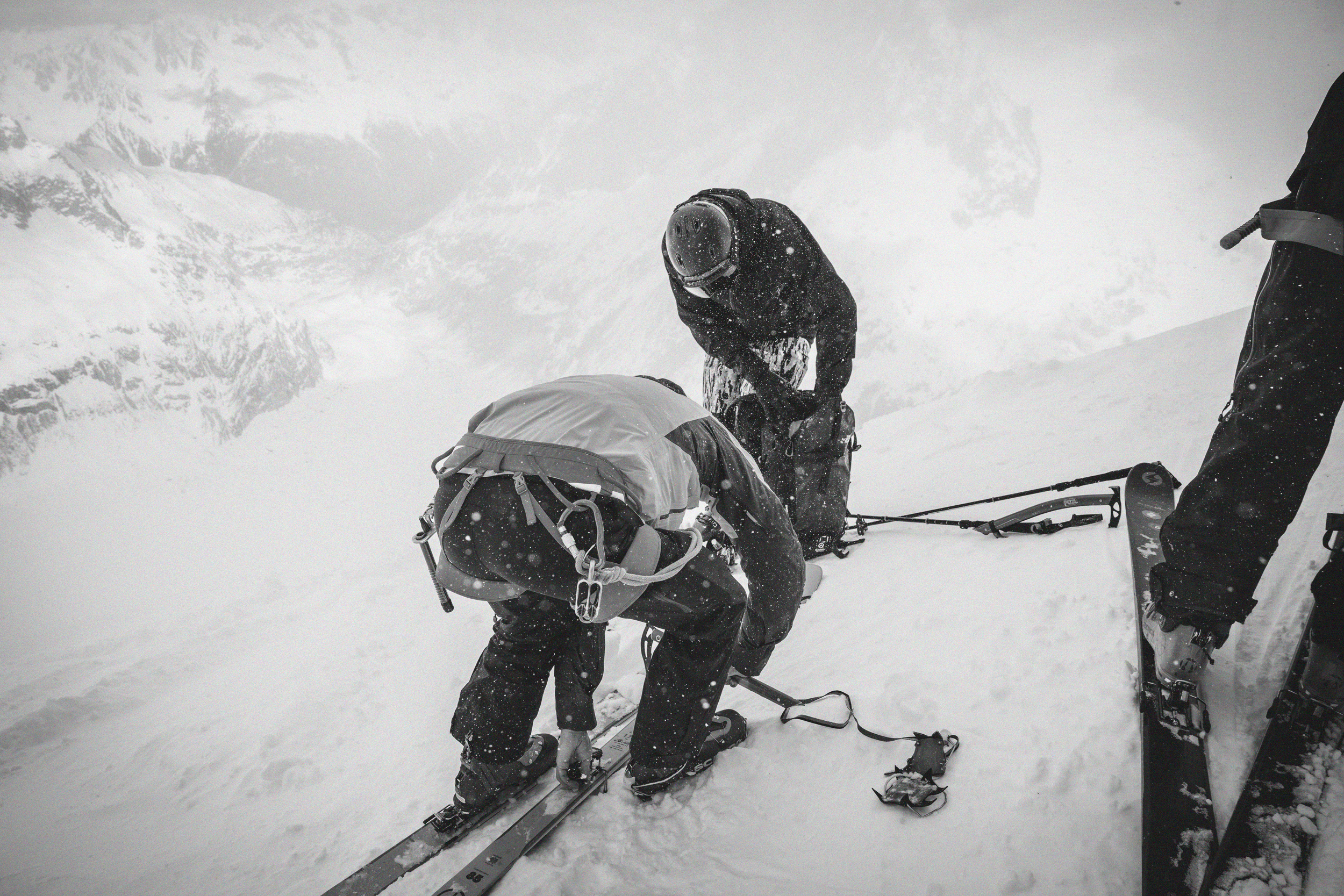 Deux personnes en vêtements de ski préparant leur équipement dans un paysage montagneux enneigé.
