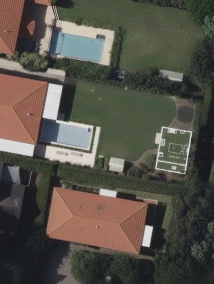 Aerial view of a residential backyard with two pools, a lawn, a sports court, and surrounding houses with red-tiled roofs.
