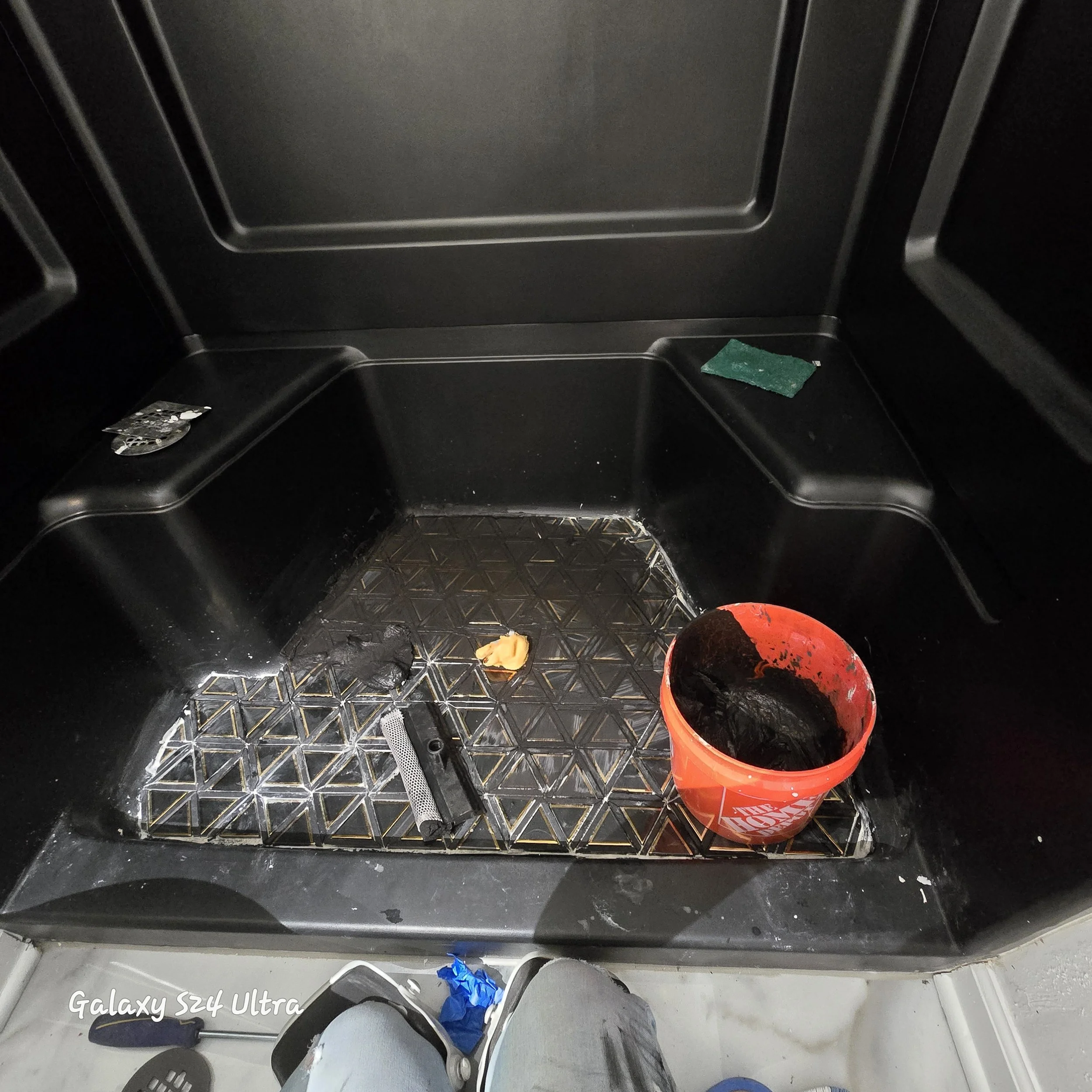 A shower floor tile installation with black and gold tile during the installation. 