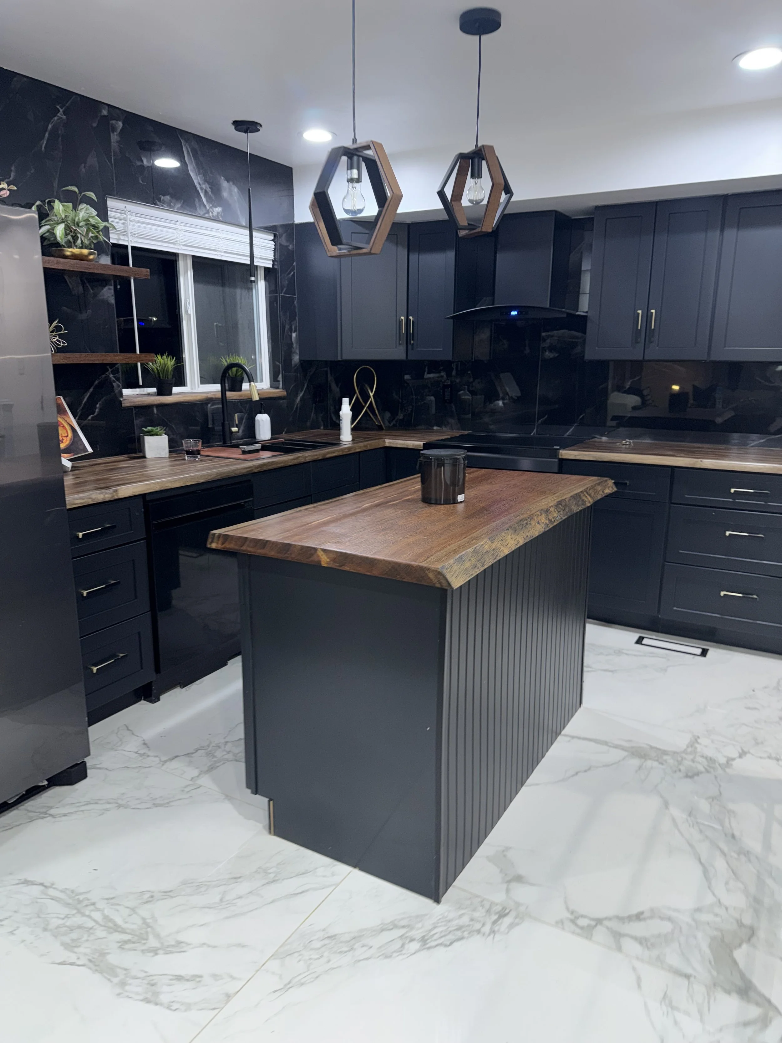 Modern kitchen with black cabinets, a wooden countertop, a black island with a wooden top, black tile backsplash, pendant lights, and marble floor tiles.