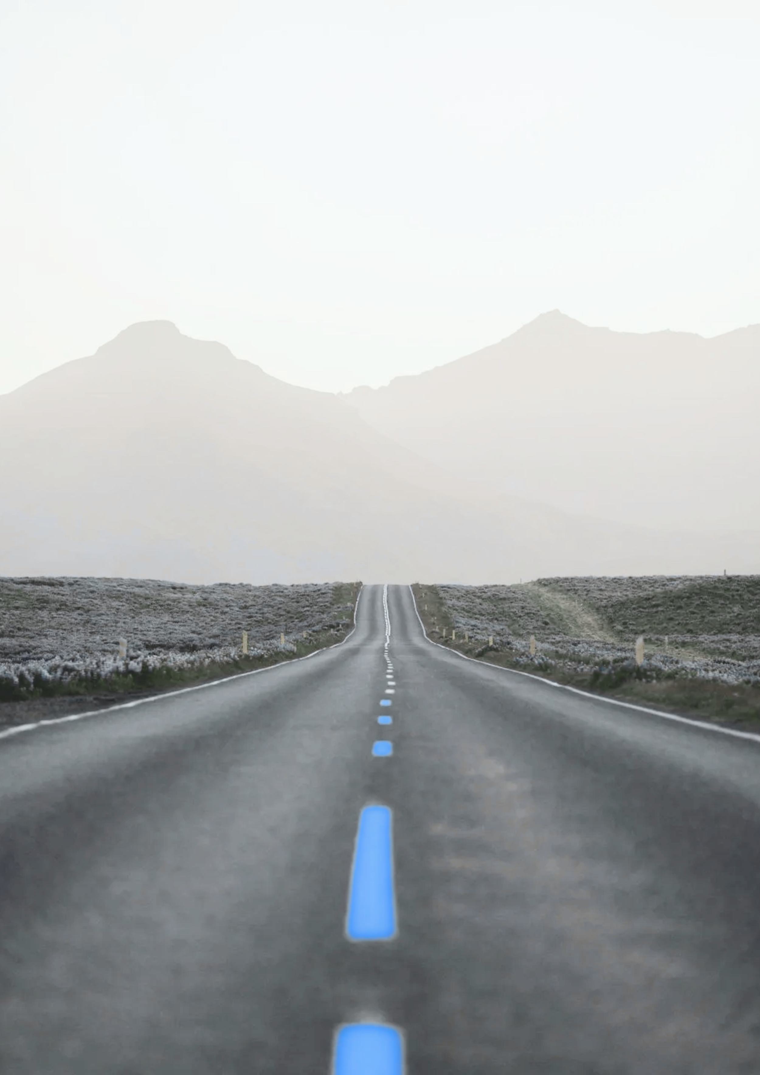 Une route droite s'étend vers l'horizon dans un paysage désertique avec montagnes en arrière-plan, sous un ciel clair.
