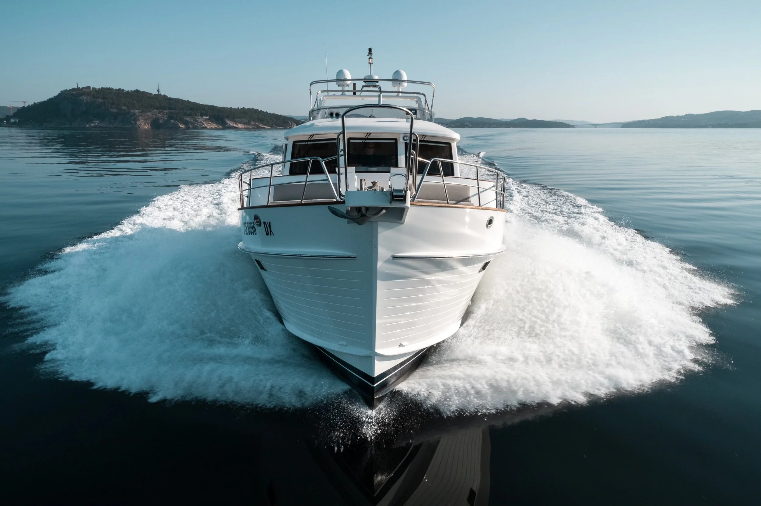 A white yacht moving through calm water with land and hills in the background.