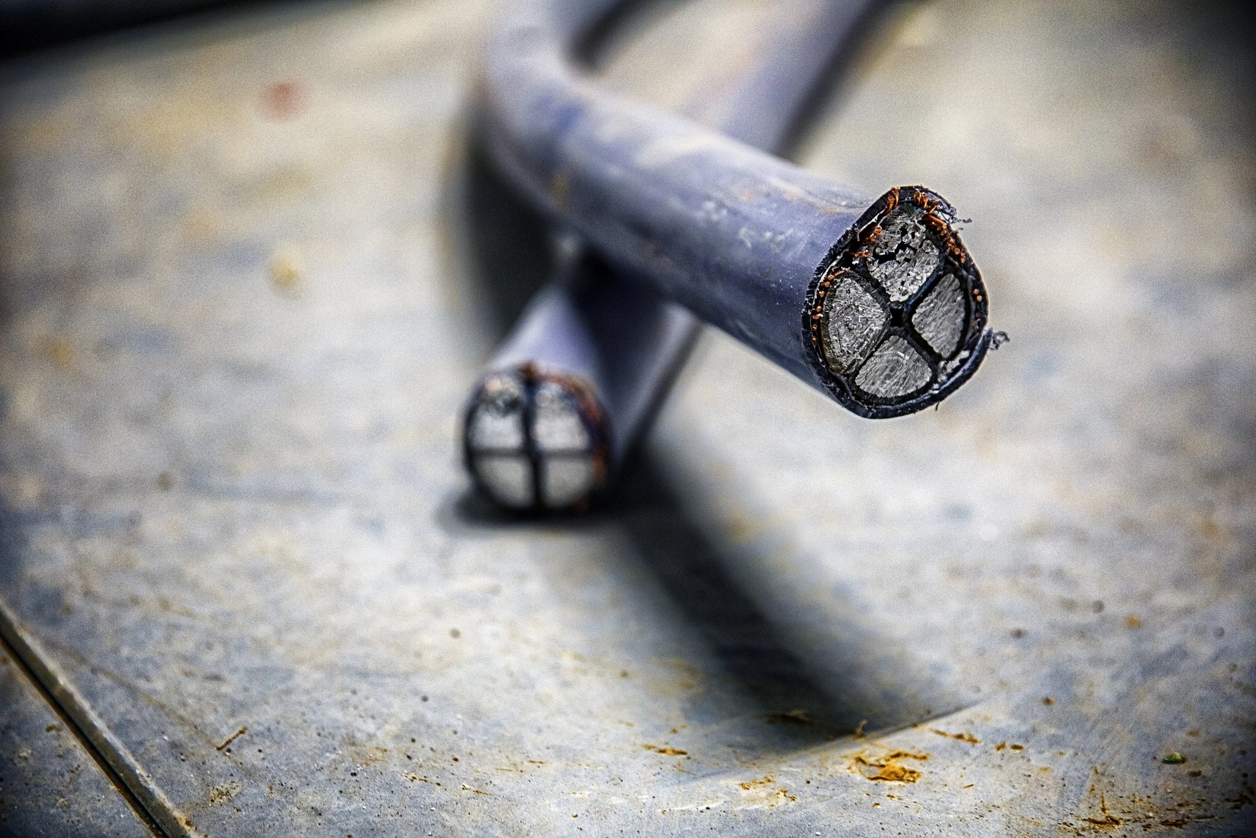 To svarte kobberrør med kuttende ender liggende på en betongflate.