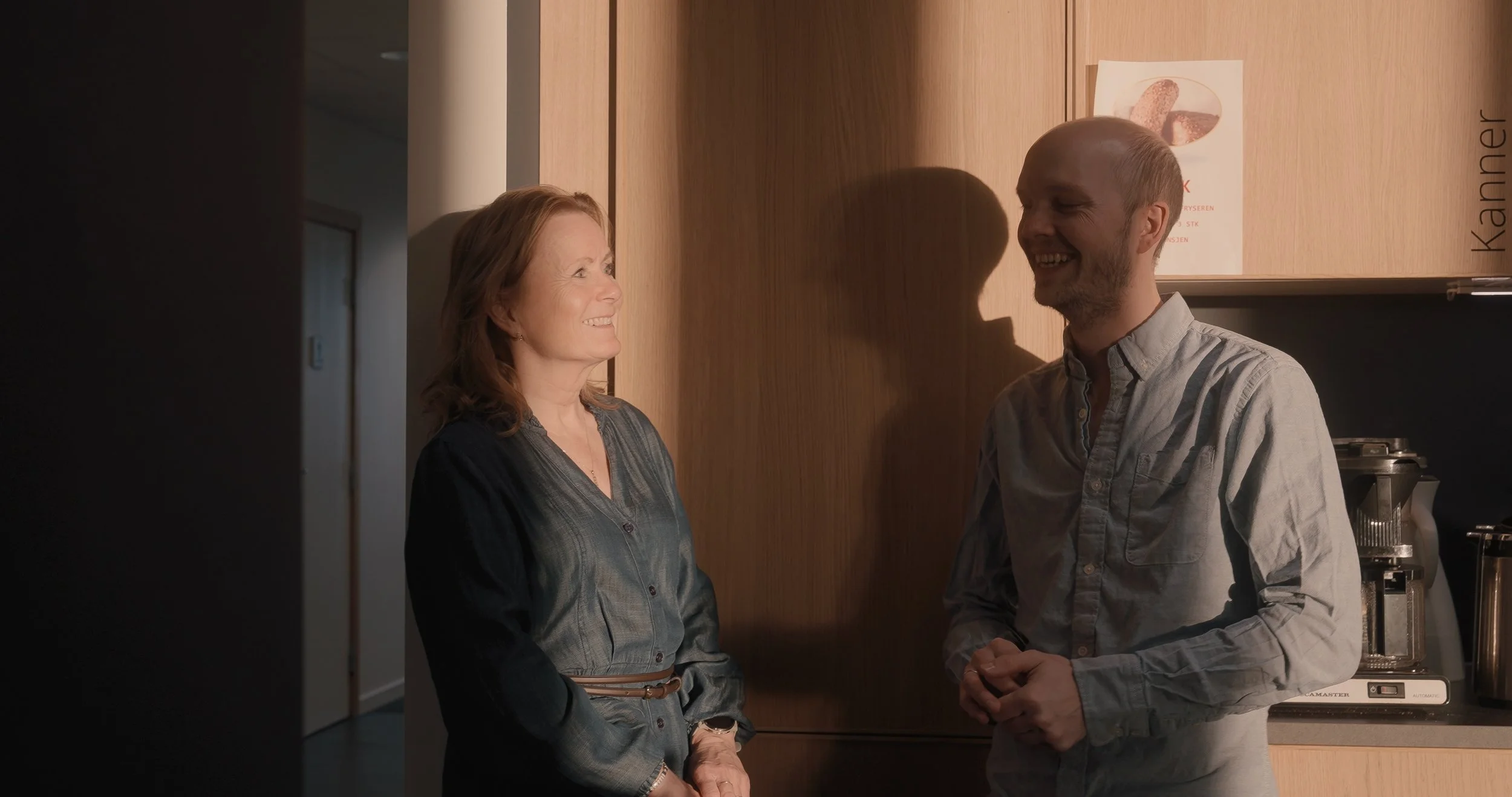 En kvinnelig og en mannlig person som står og snakker i et kjøkken.