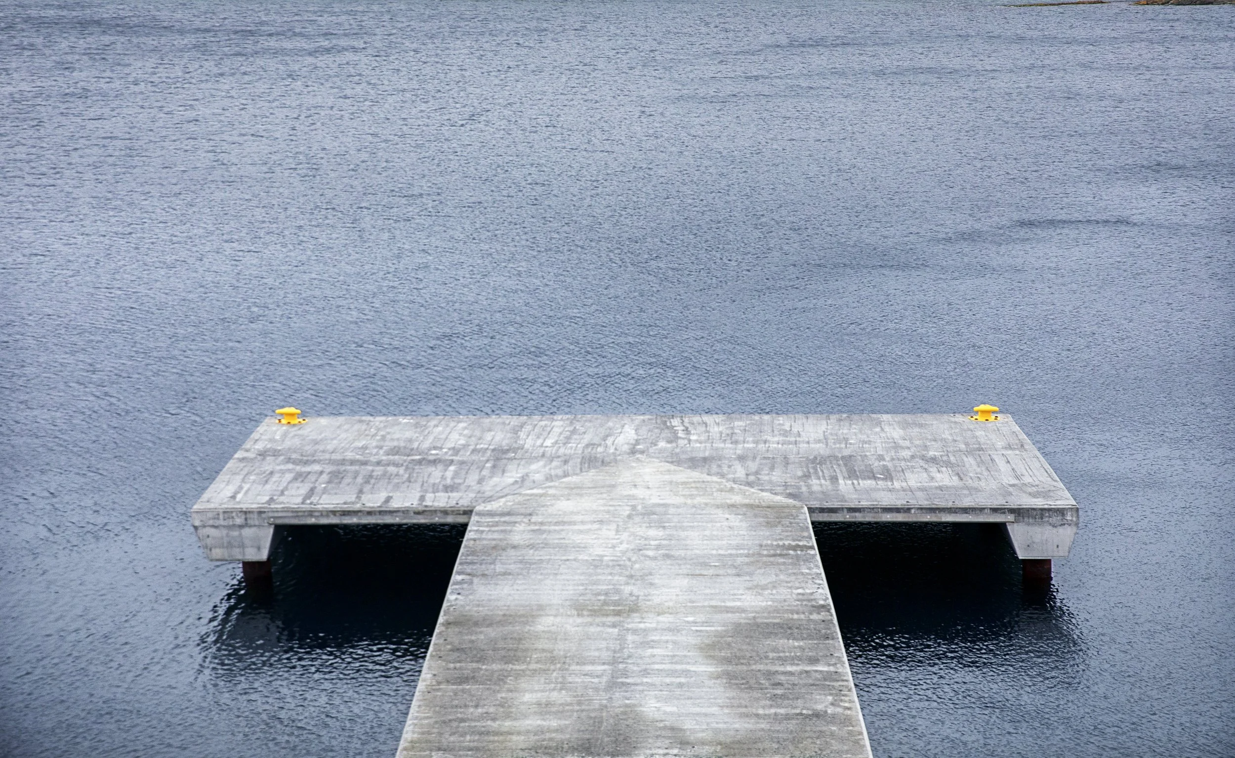 Bilde av en lang, enkel damkjetting som strekker seg ut i vannet, med to små gule fenderklosser på enden.
