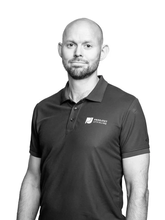 En mann iført svart polo med logoen 'Prosjekt Utvikling' foran, stående mot en hvit bakgrunn.
