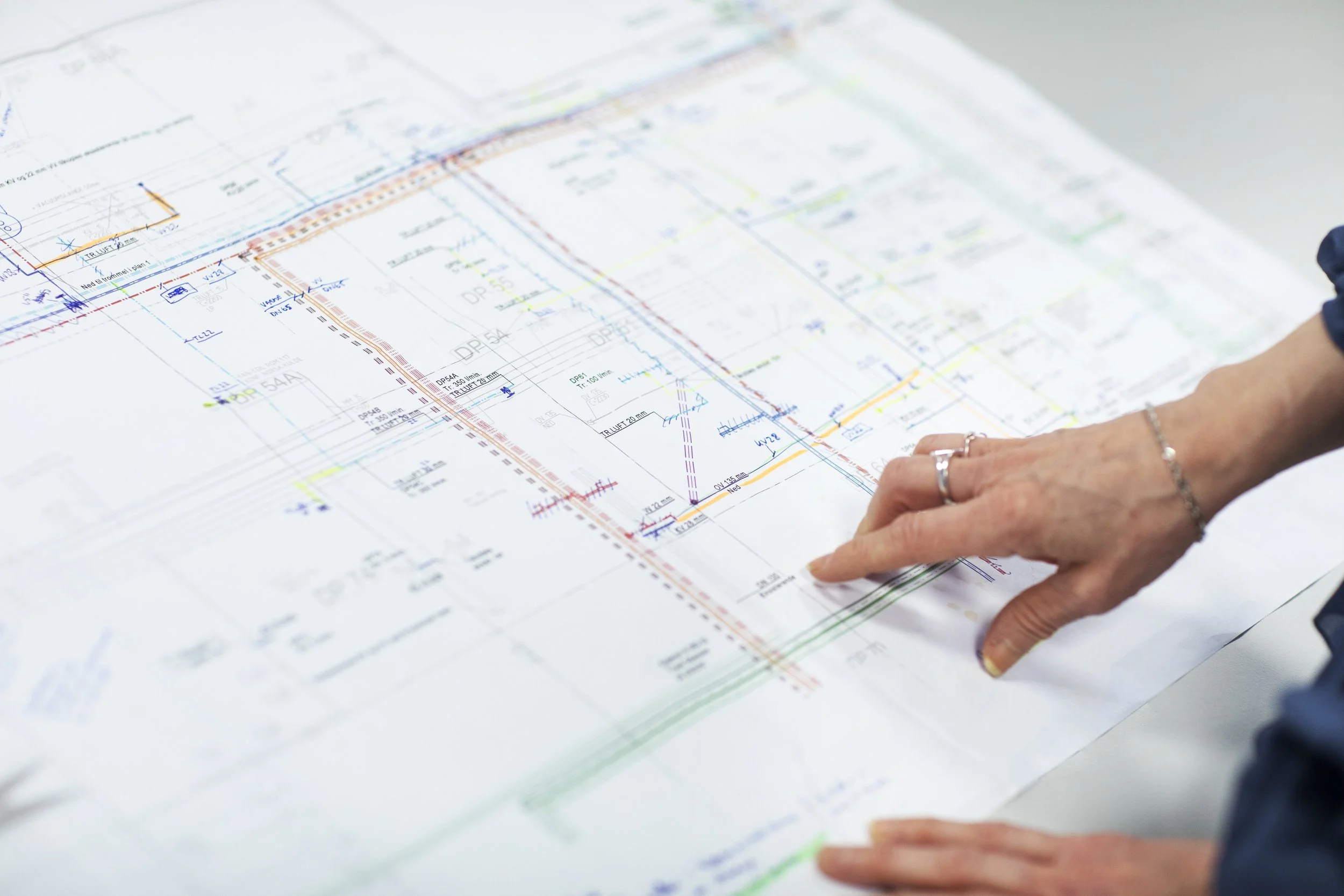 Nærbilde av et ark med tekniske tegninger og fargerike linjer, der en person peker på en del av diagrammet.
