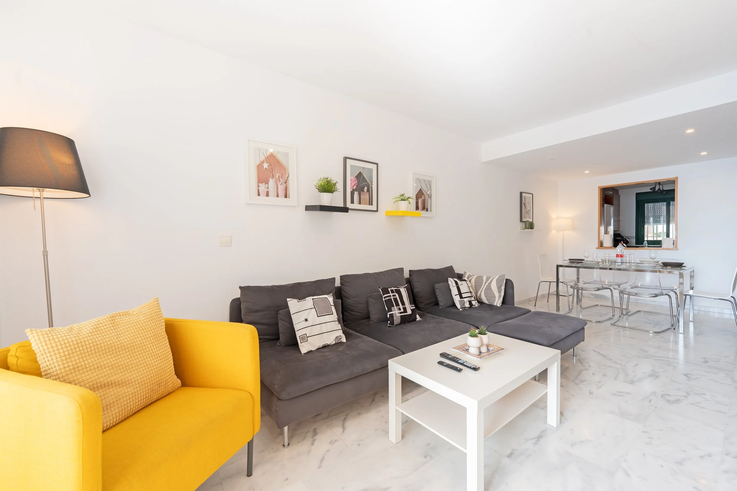Modern living room with yellow armchair, gray sectional sofa, white coffee table, and artistic wall decor.