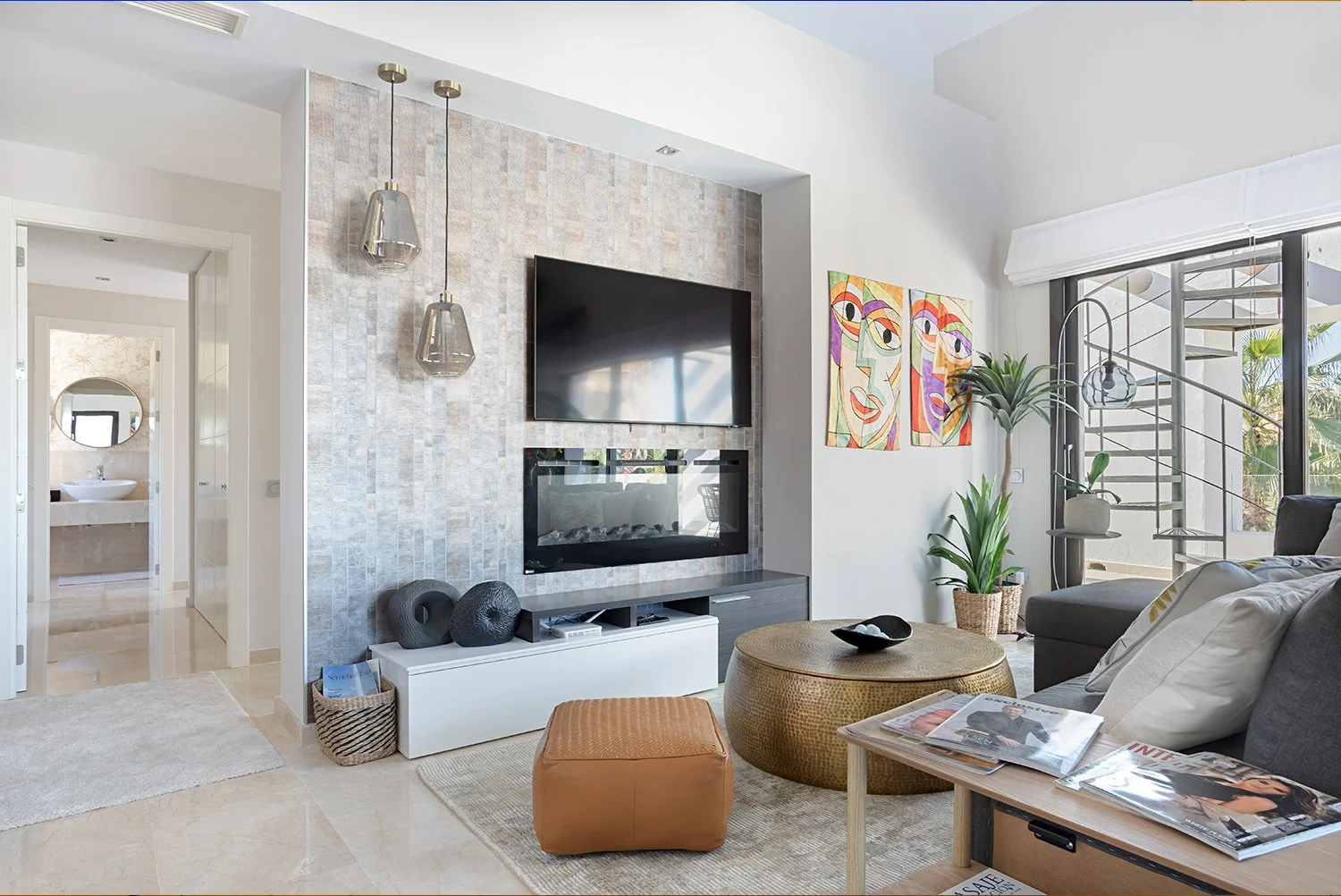 A modern living room with a wall-mounted flat-screen TV and electric fireplace, decorated with abstract art, plants, and contemporary furniture.