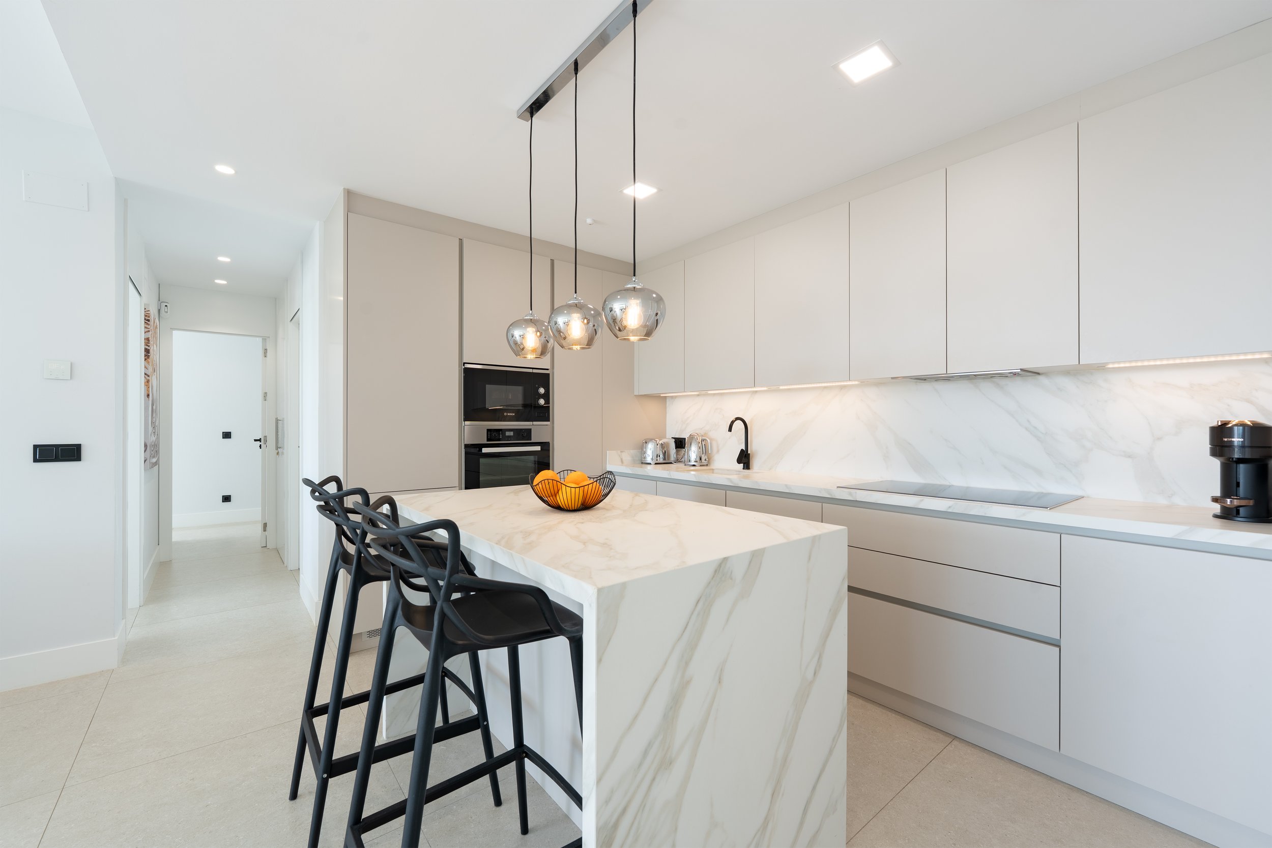 Modern kitchen with white marble island, light grey cabinets, black pendant lights, and black bar stools