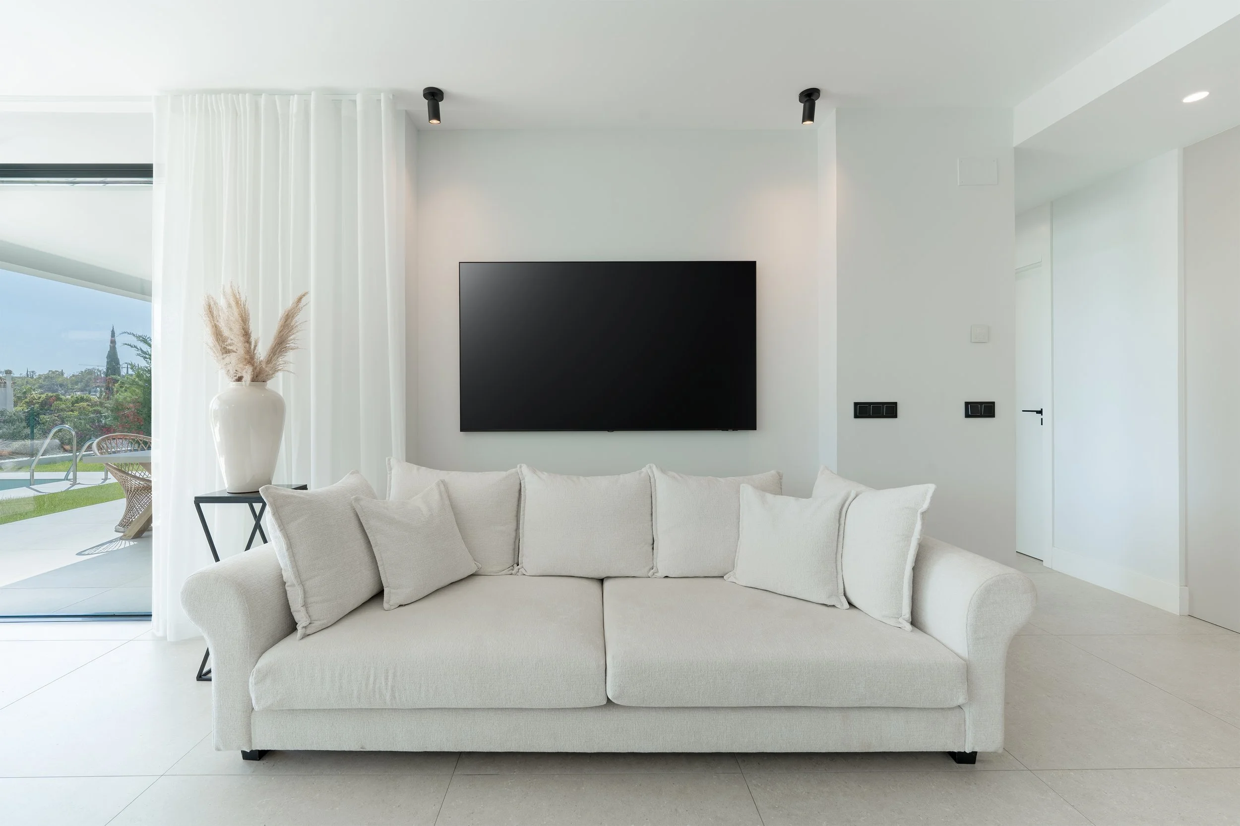 Minimalist living room with a white sofa, TV on the wall, and large window with a view of the outdoors.