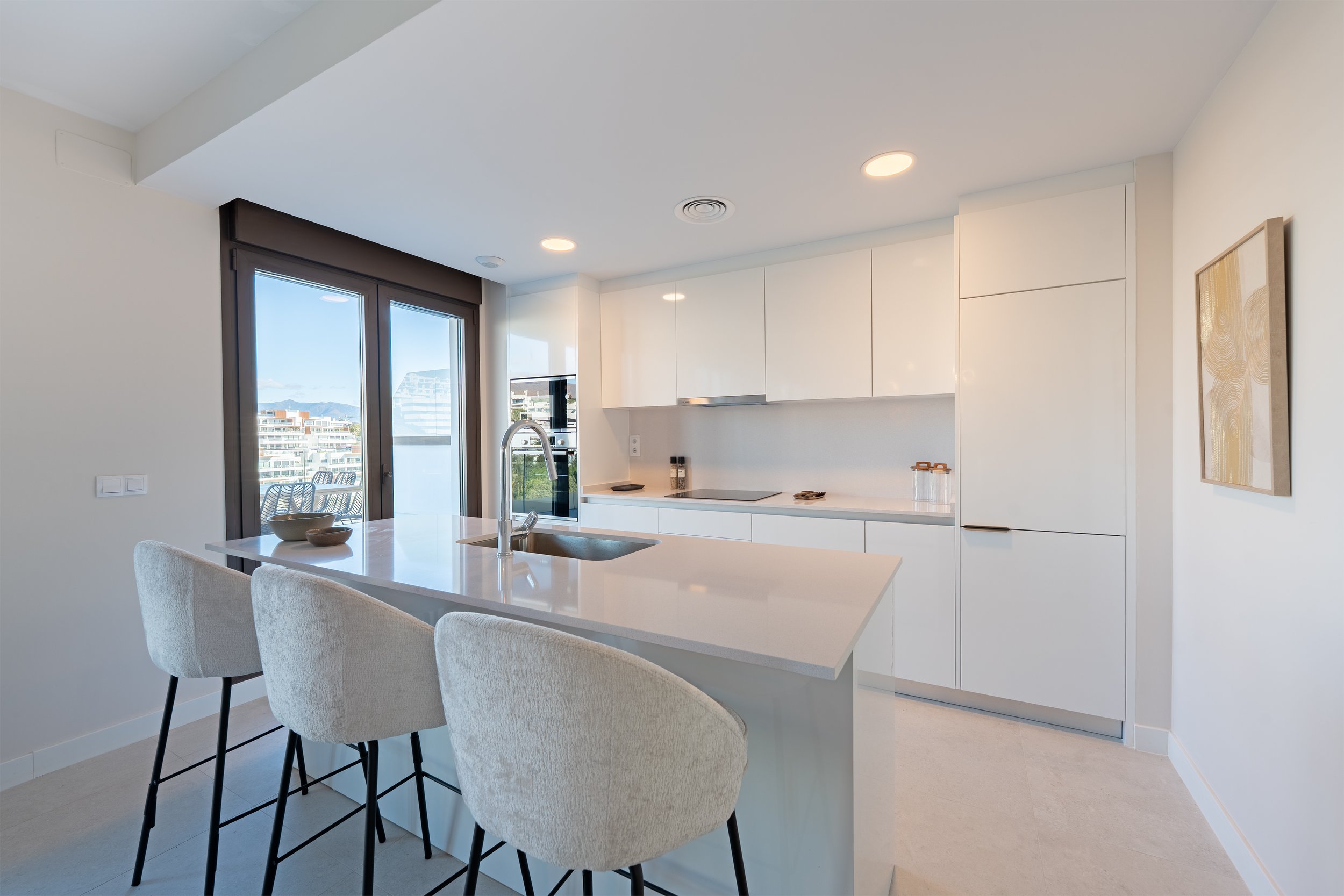 Modern kitchen with white cabinetry, a kitchen island with seating, large windows with city views, and minimal decor.