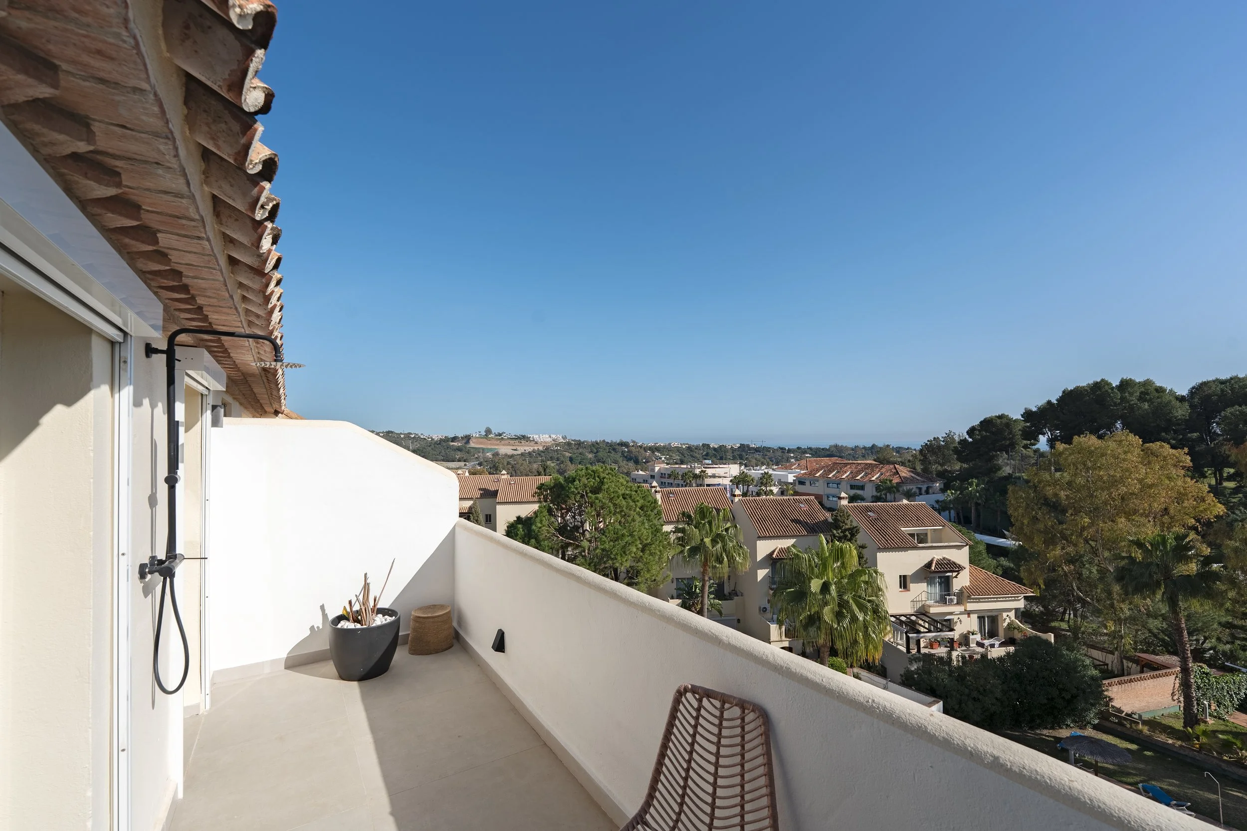 Balcony with potted plant, outdoor shower, and view of suburban neighborhood with trees and rooftops