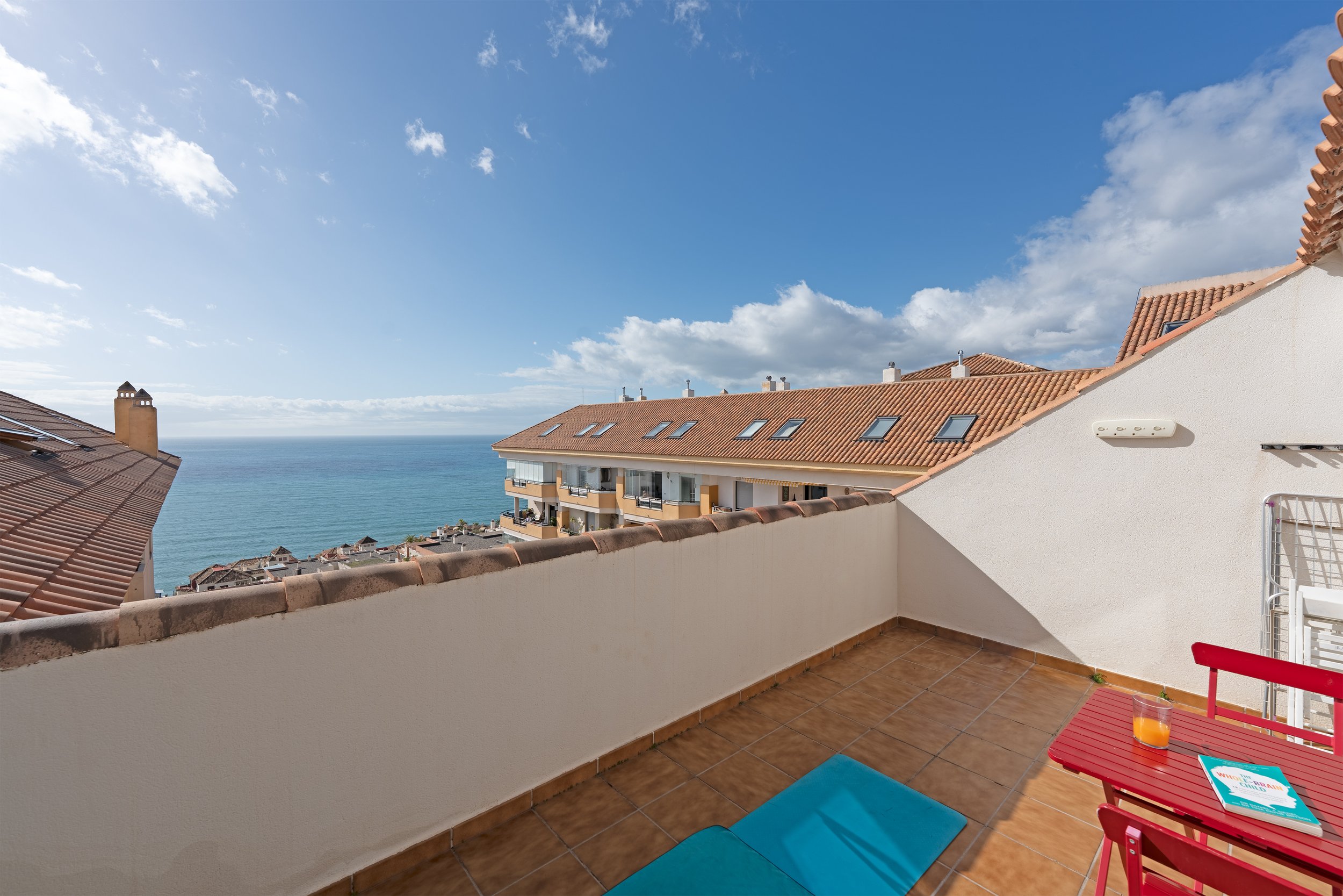 Balcony overlooking rooftops and the ocean with partly cloudy sky
