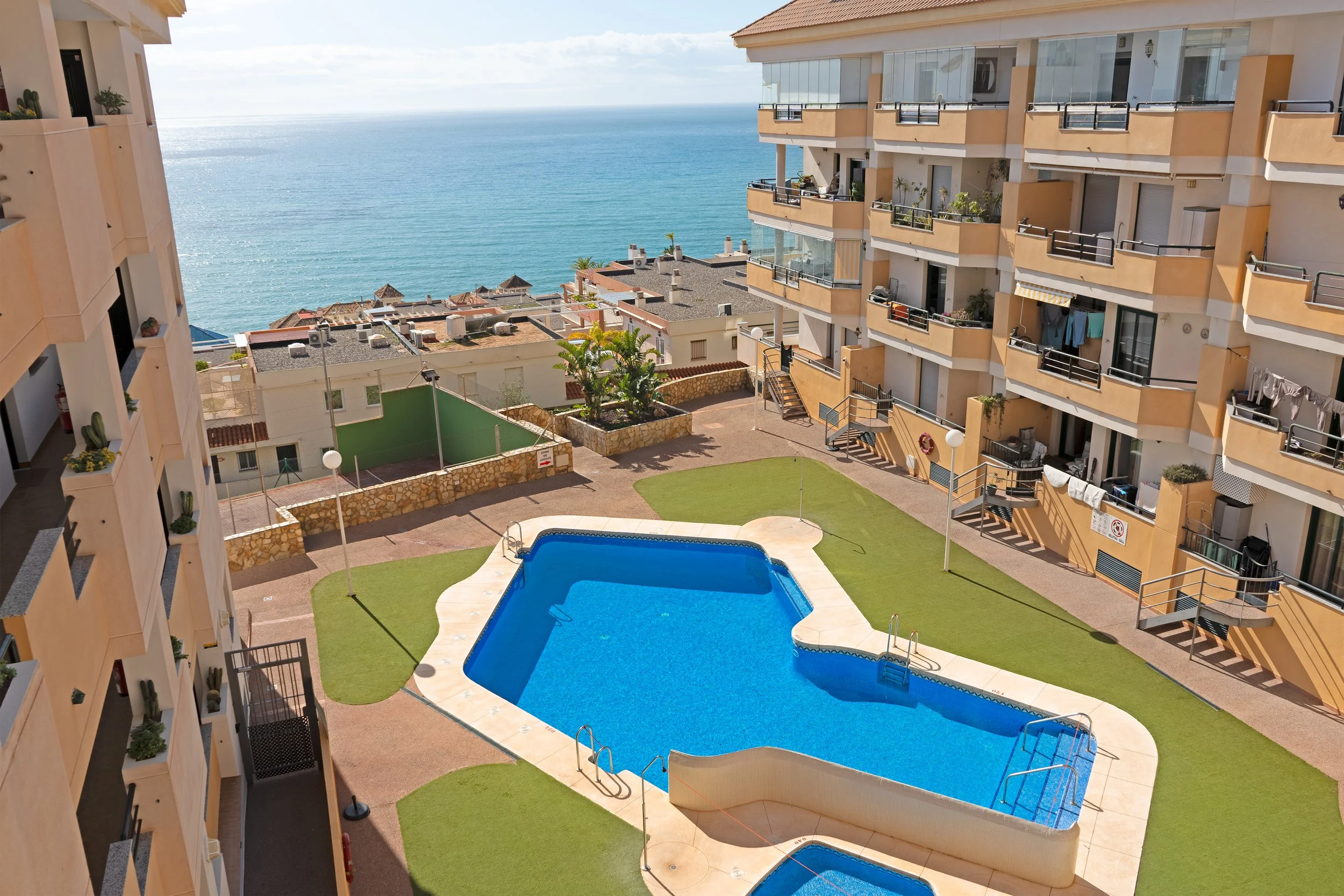 View of a swimming pool in a residential complex with ocean in the background.