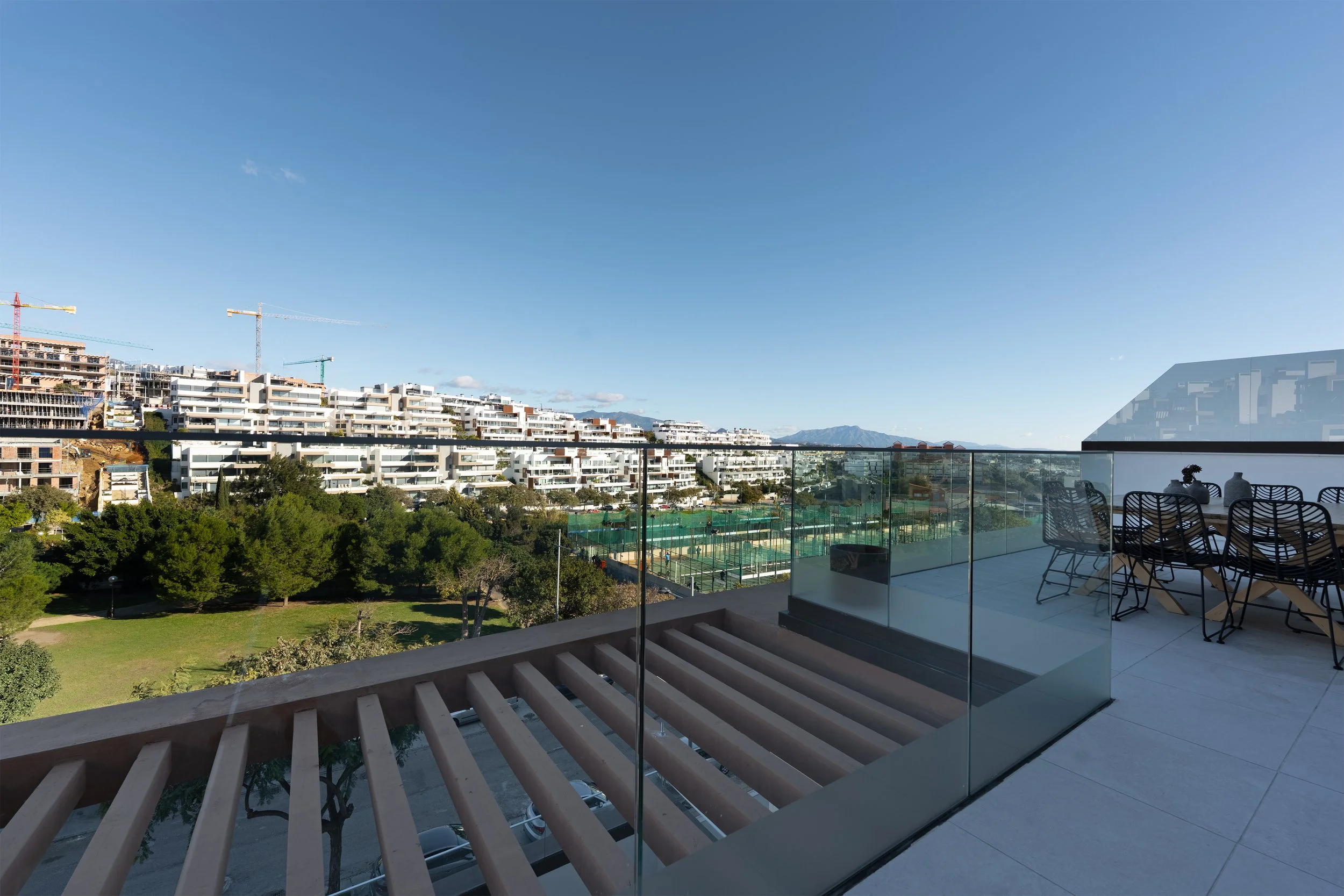 View from a balcony showing a golf course, trees, a modern apartment complex under construction, and a mountain range in the distance.