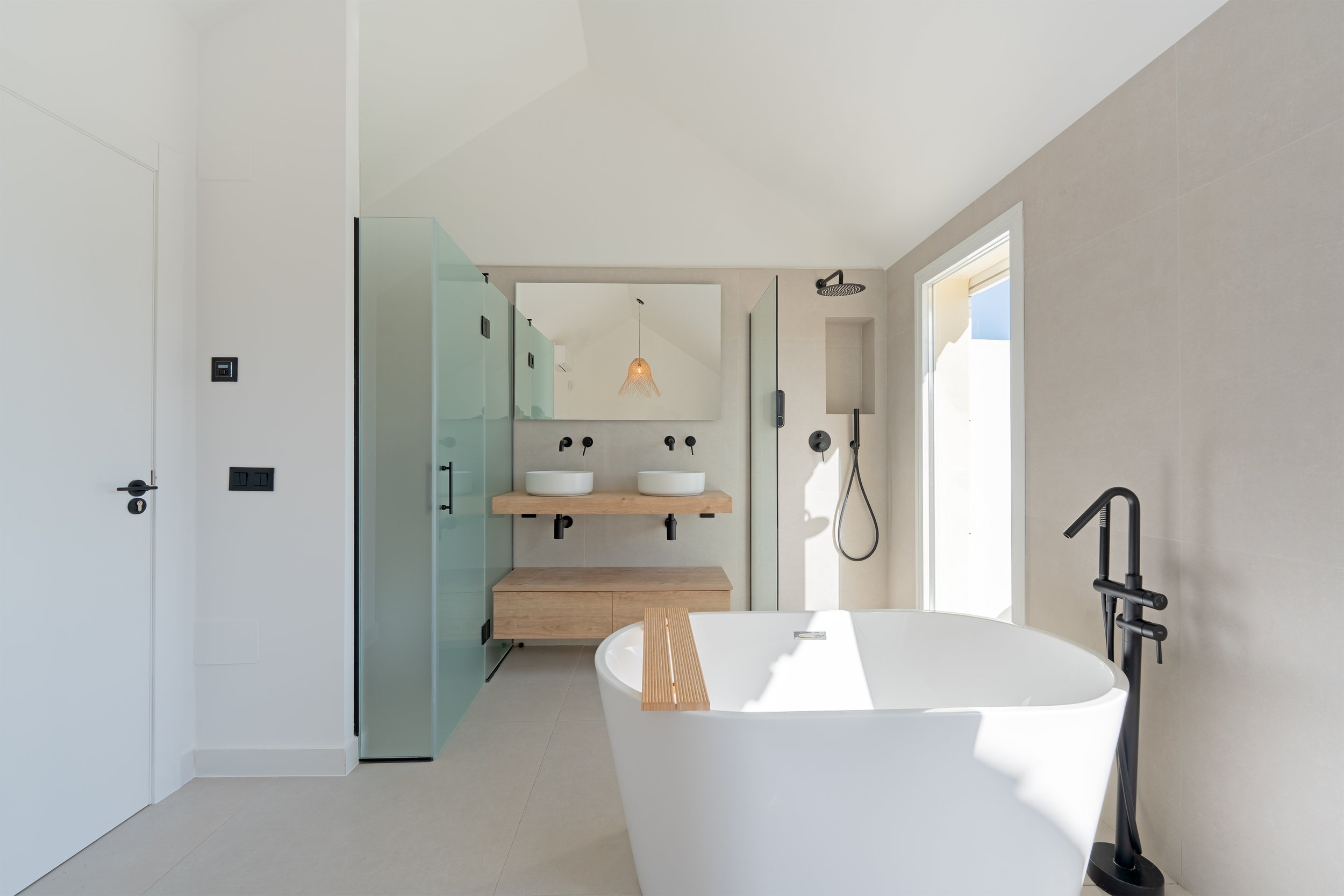 Modern bathroom with freestanding bathtub, dual sinks on a wooden vanity, walk-in shower, large mirror, and natural light.