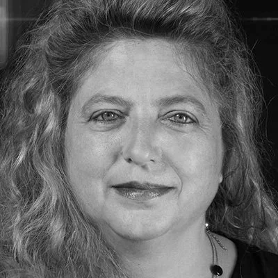 Schwarz-weiß Porträt einer Frau mit lockigem Haar, die direkt in die Kamera schaut.