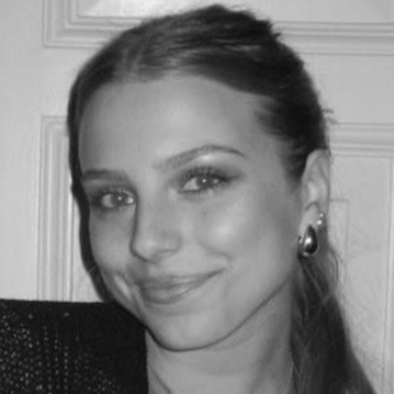 Schwarz-Weiß-Foto einer lächelnden jungen Frau mit glatten, langen Haaren, die in ein Ohr ein Ohrring trägt.