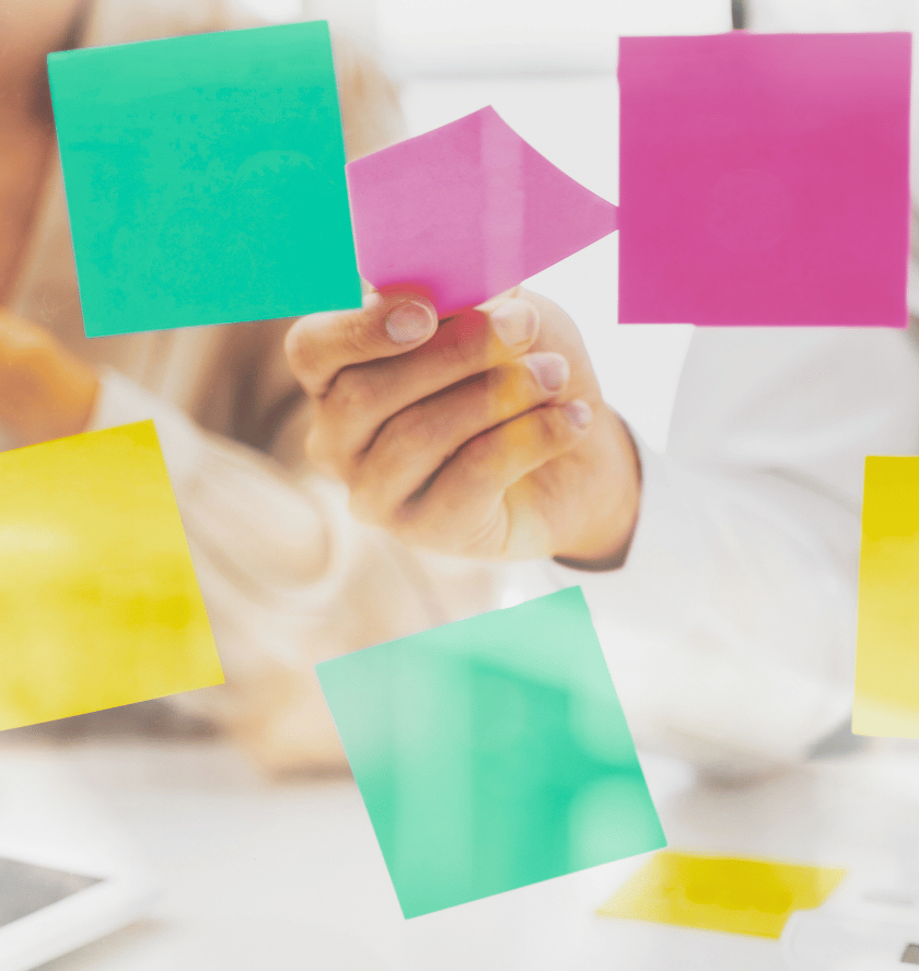 Person hält bunte Haftnotizen auf einer Glaswand im Büro.
