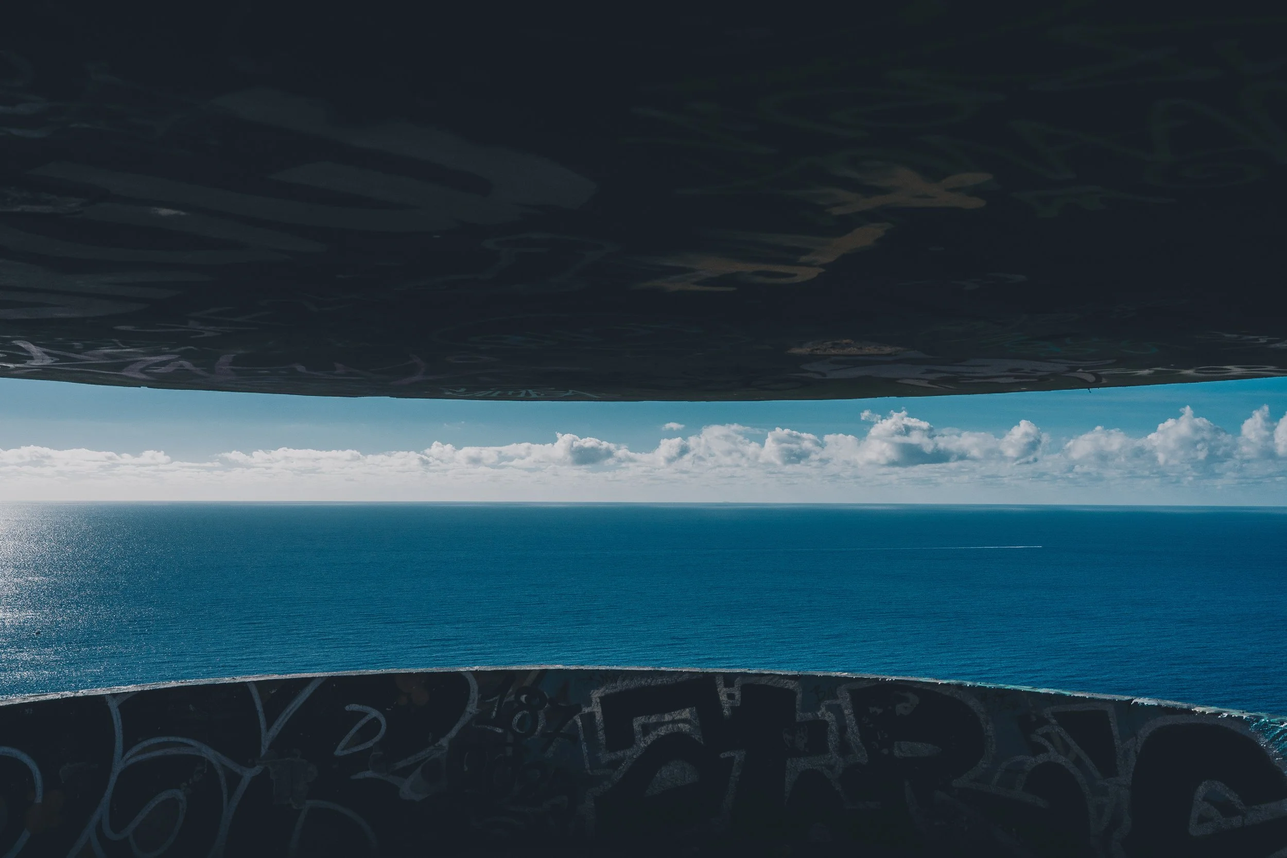 Vue de l'océan entre deux structures sombres, avec un ciel bleu et des nuages blancs.