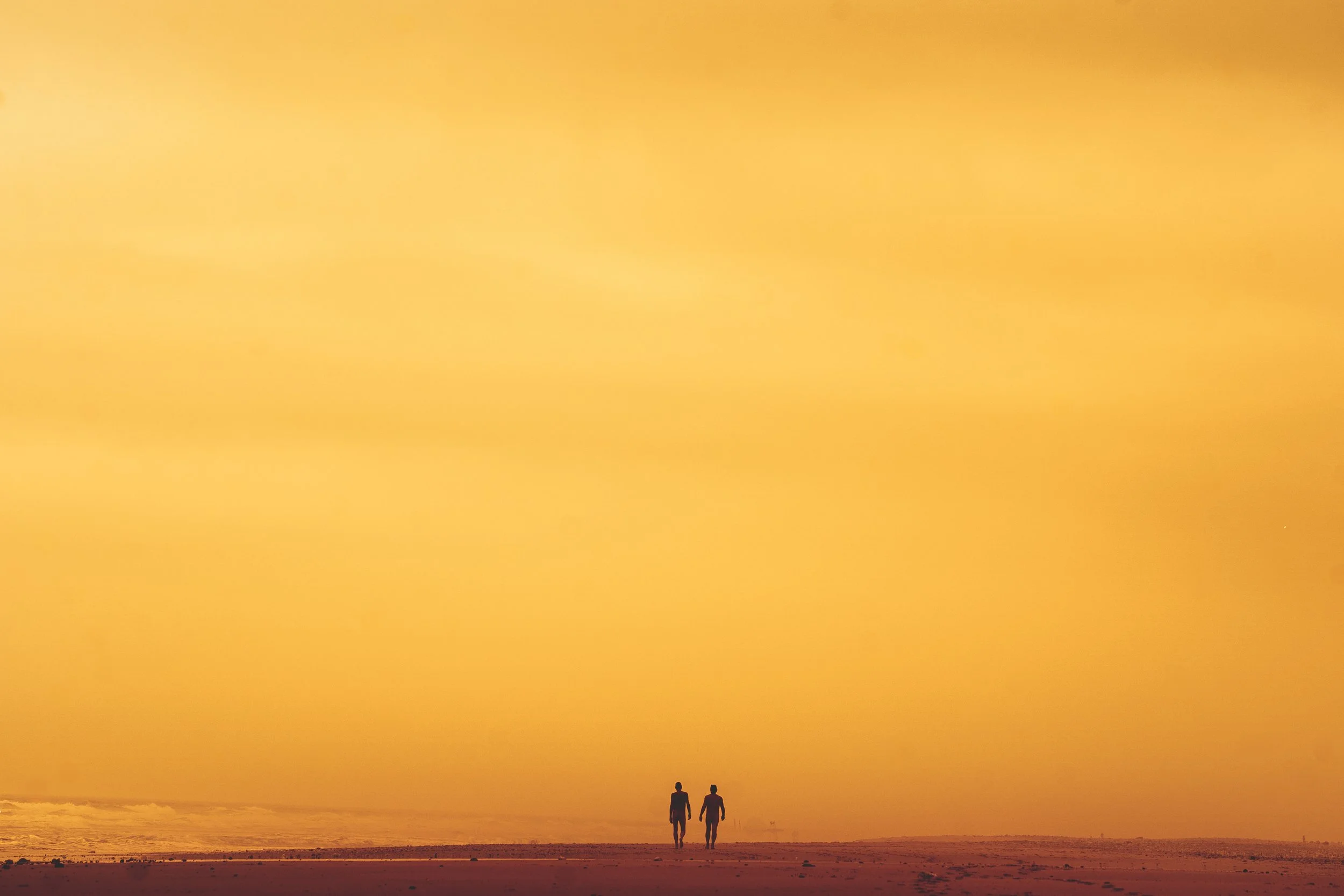 Deux personnes marchant sur la plage au coucher du soleil, ciel orange