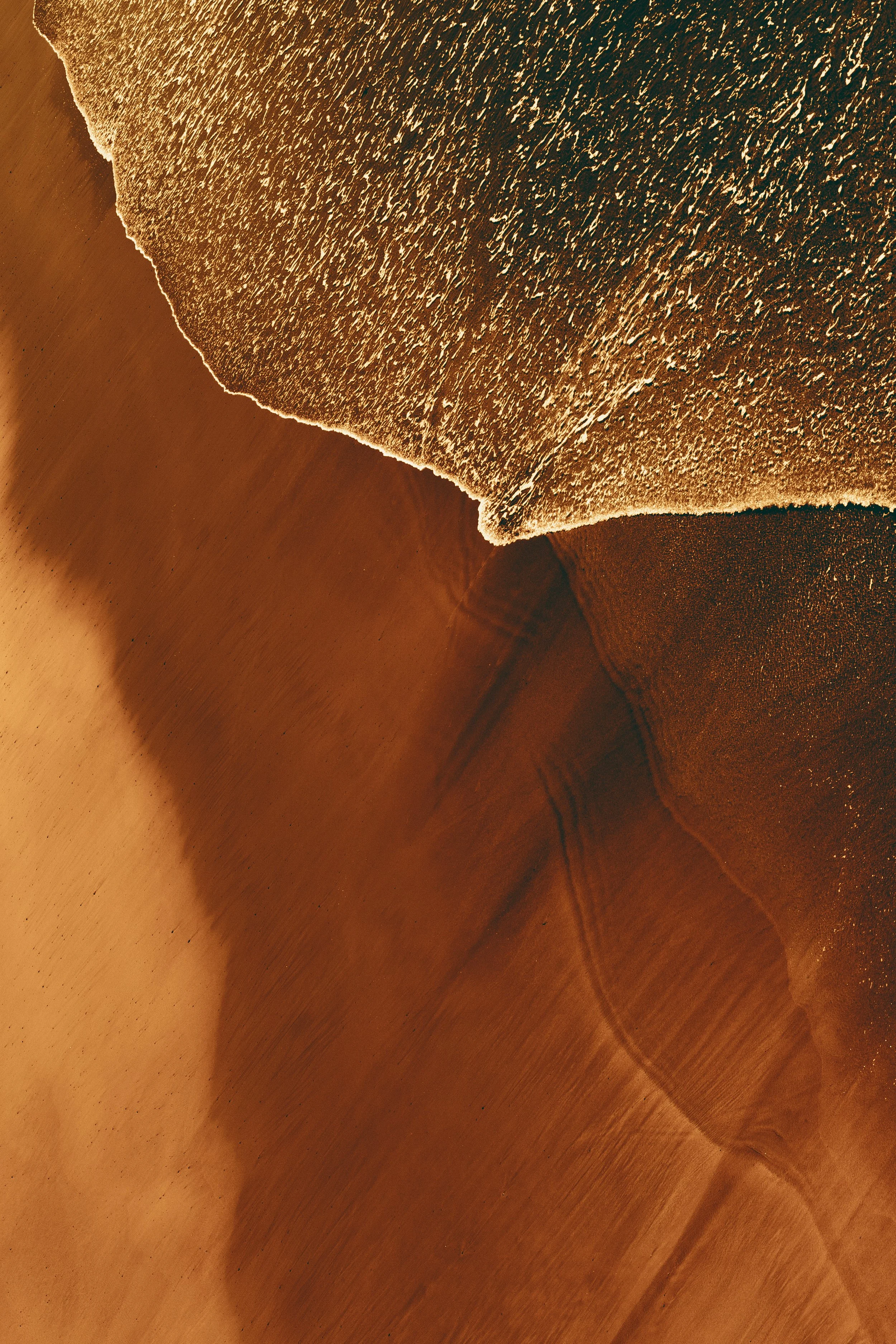 Photo aérienne d'une plage de sable doré avec des vagues se brisant sur le rivage, vue depuis le ciel.