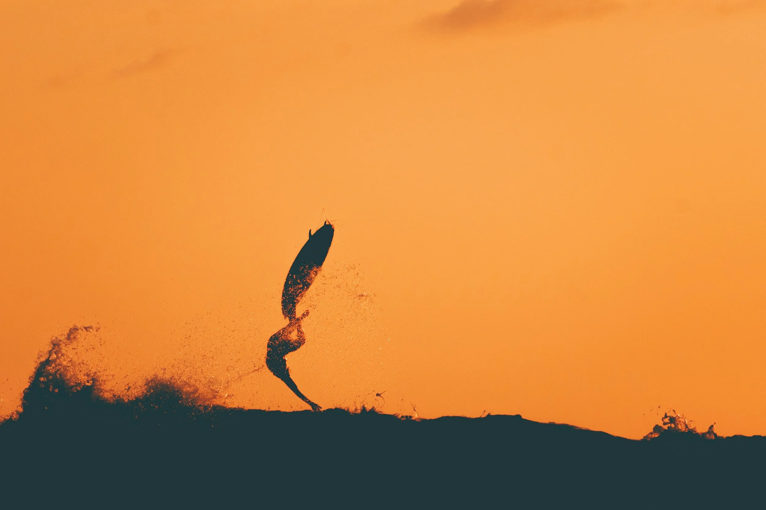 Silhouette d'une personne a la plage au coucher du soleil, lançant un objet dans les airs, avec un ciel orange en arrière-plan.