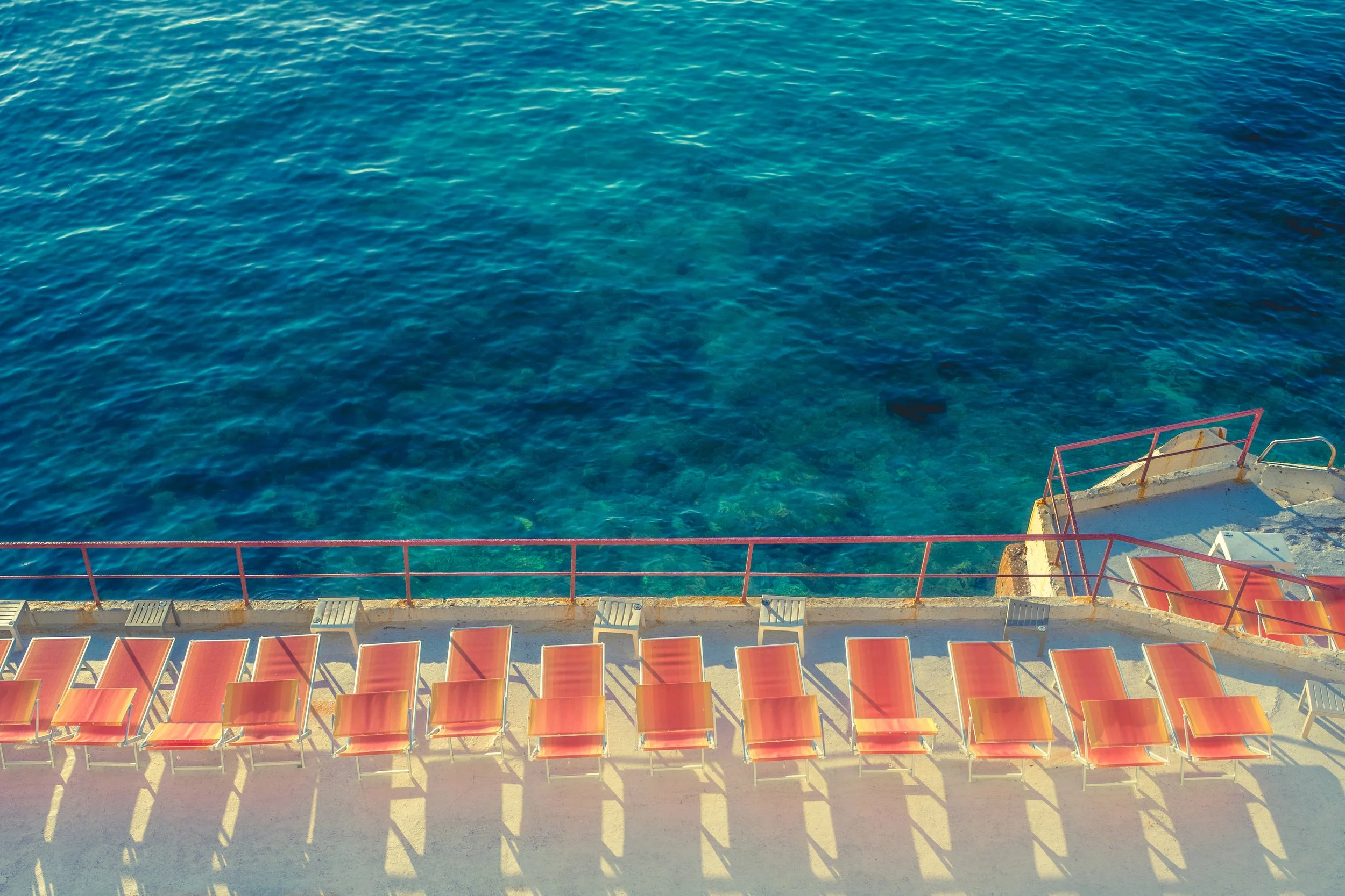 Chaises longues orange sur une terrasse au bord de la mer, vue aérienne.