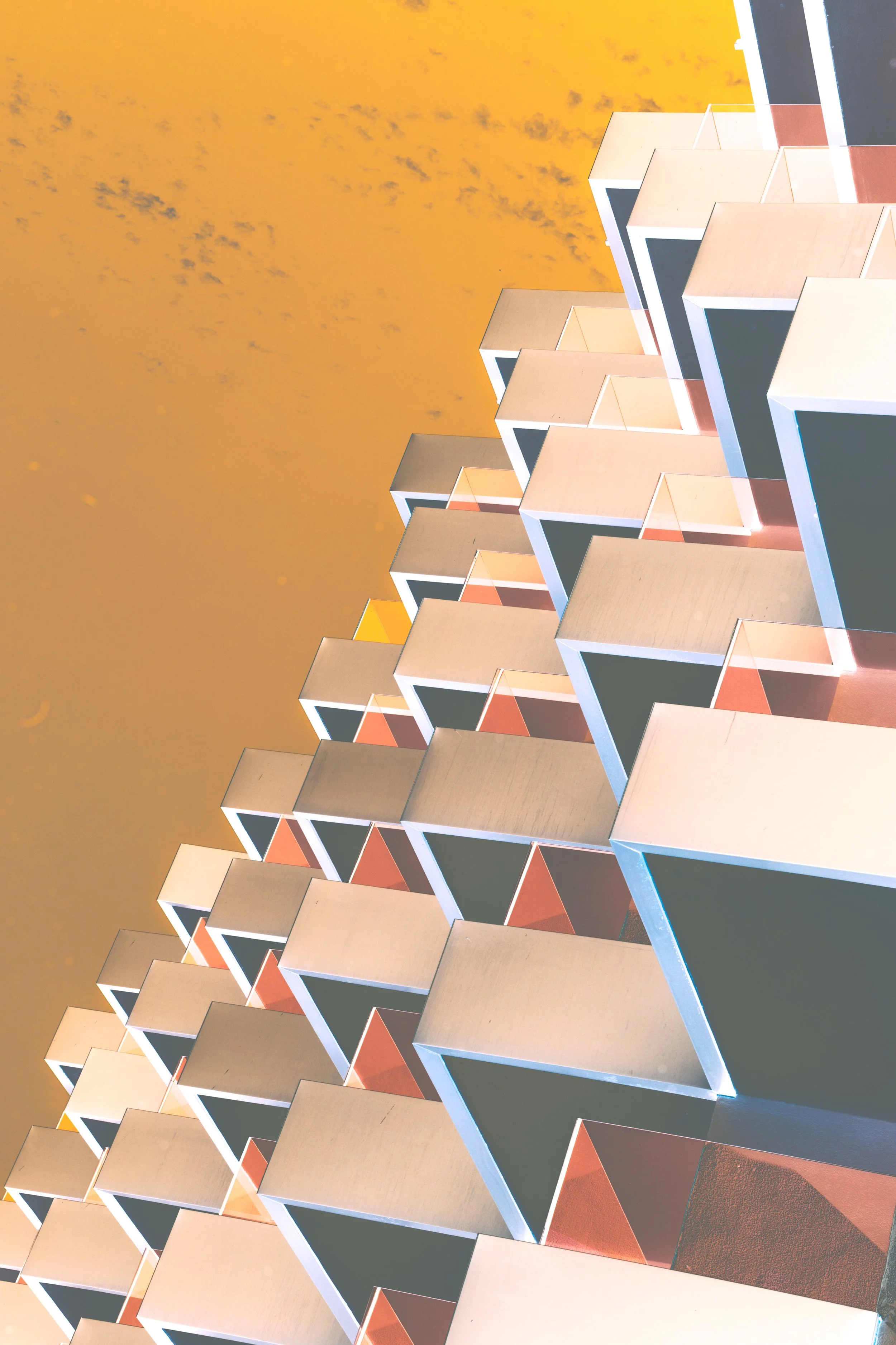 Façade d'un immeuble moderne avec des balcons en forme de cubes disposés en rangée, vue en contre-plongée, ciel orange en arrière-plan.