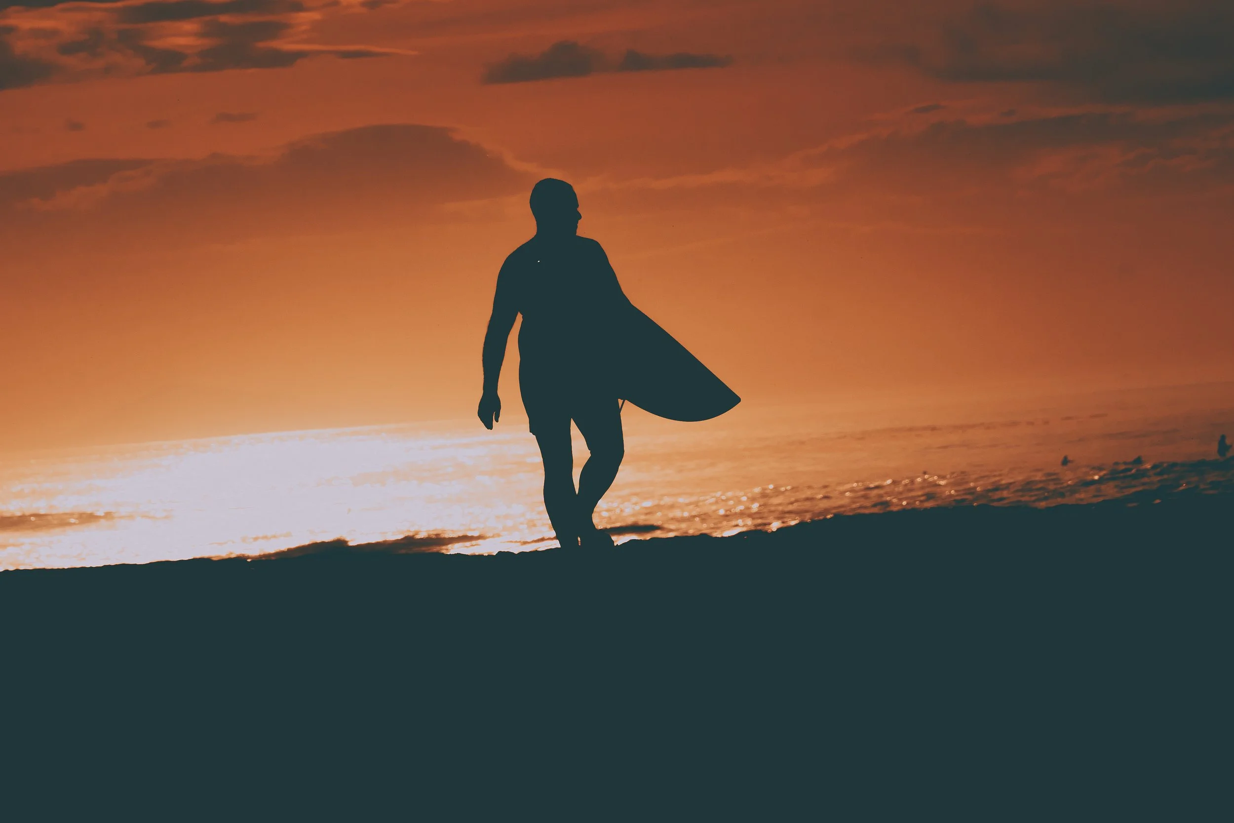Silhouette d'un surfeur marchant sur la plage au coucher du soleil