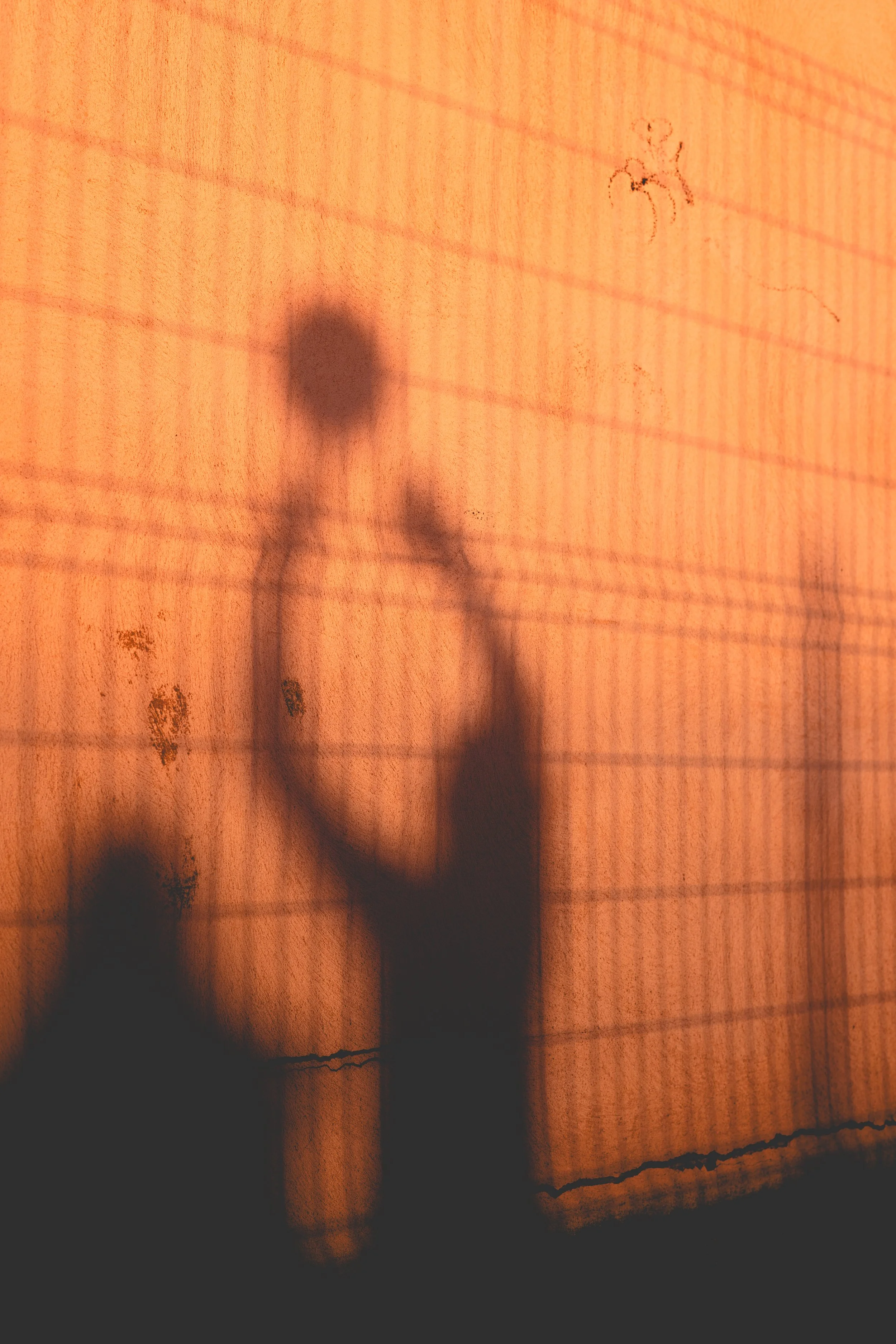 Ombres d'une personne se reflétant sur une surface en verre ou en plastique avec une lumière orangée et des lignes horizontales.