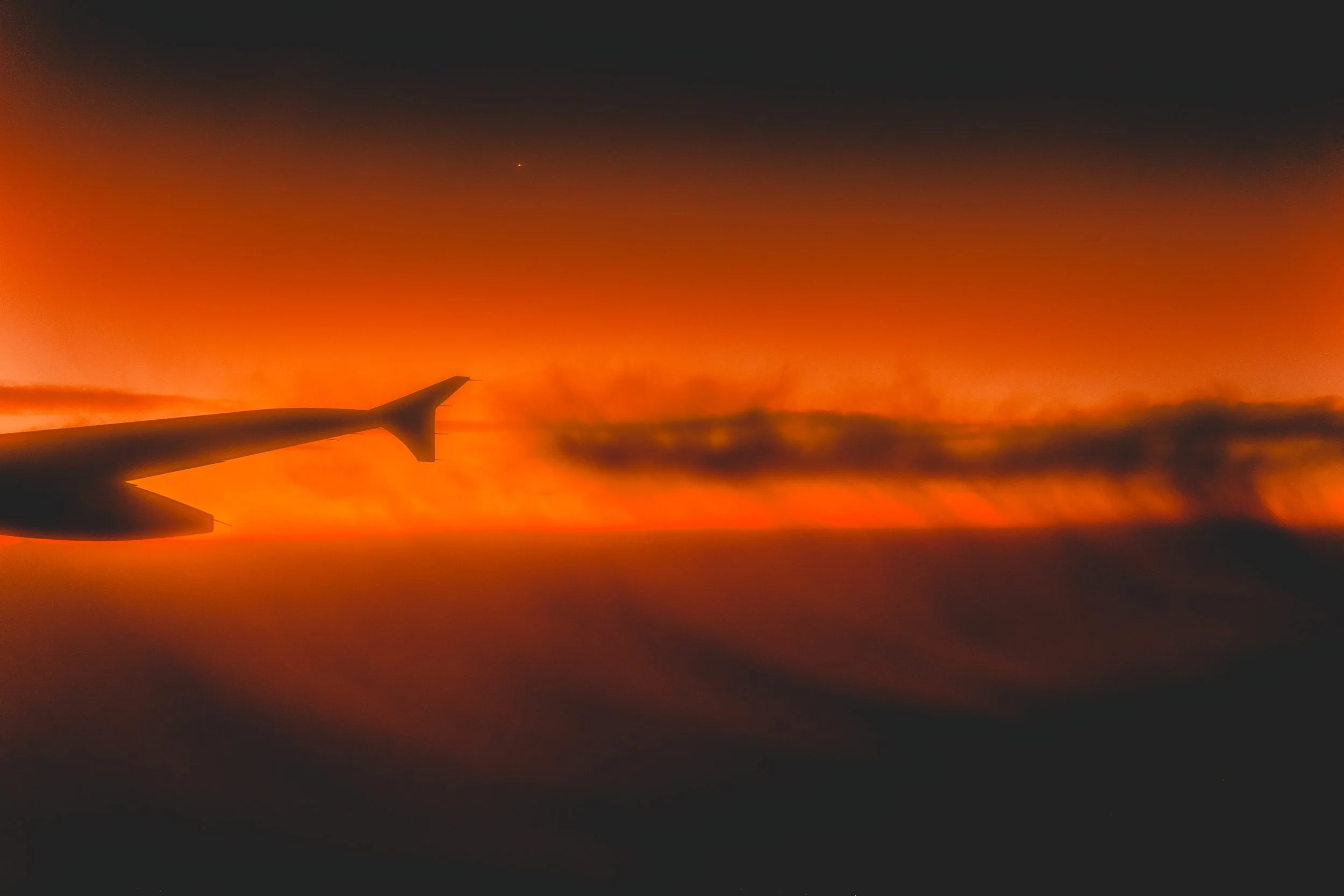 Vue d'un avion en vol au-dessus des nuages lors d'un coucher de soleil ou d'un lever de soleil avec des couleurs chaudes et un ciel en dégradé allant du rouge à l'orange.