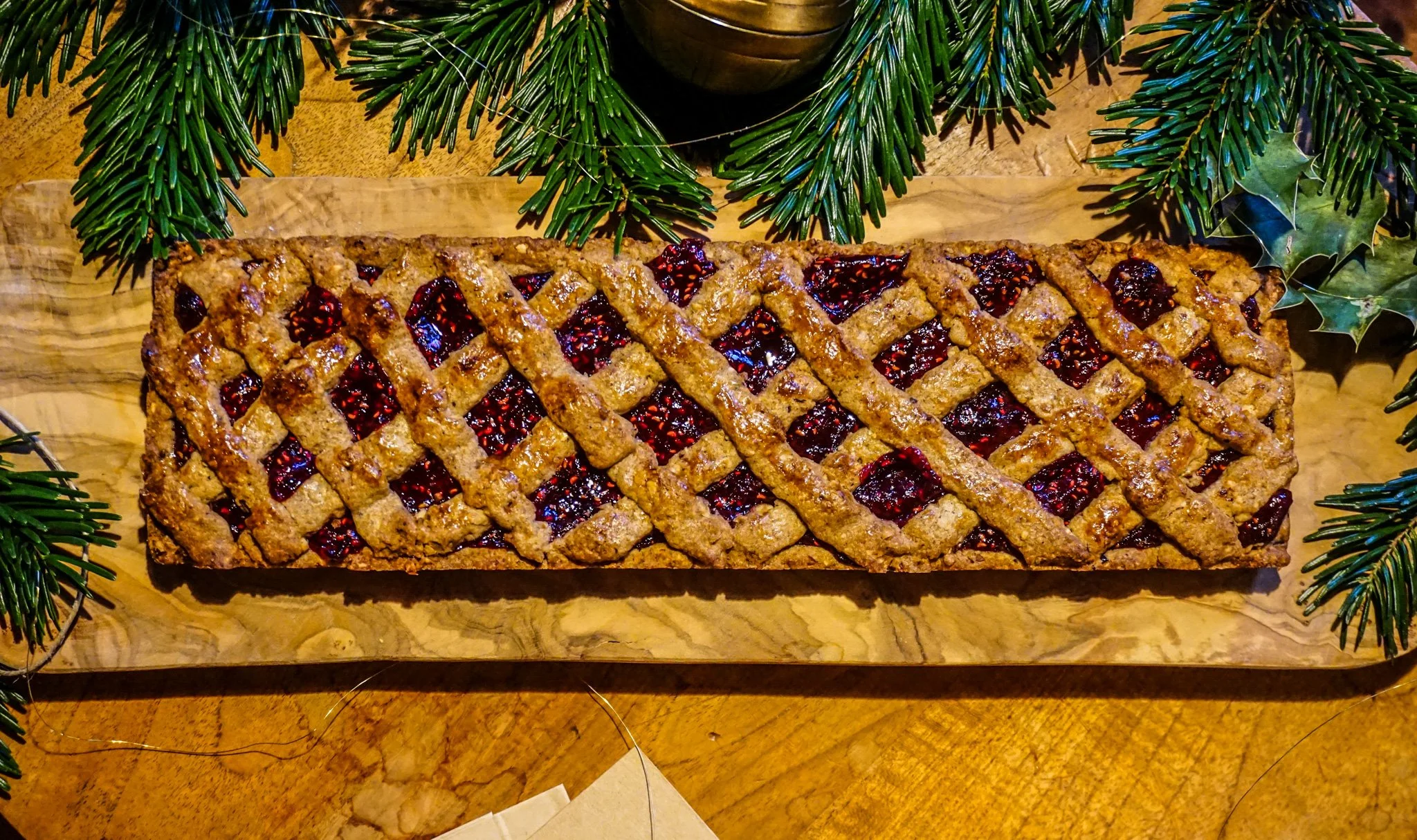 Streuselkuchen mit Beeren und Zimt auf einem Holzbrett, umrahmt von Tannenzweigen.