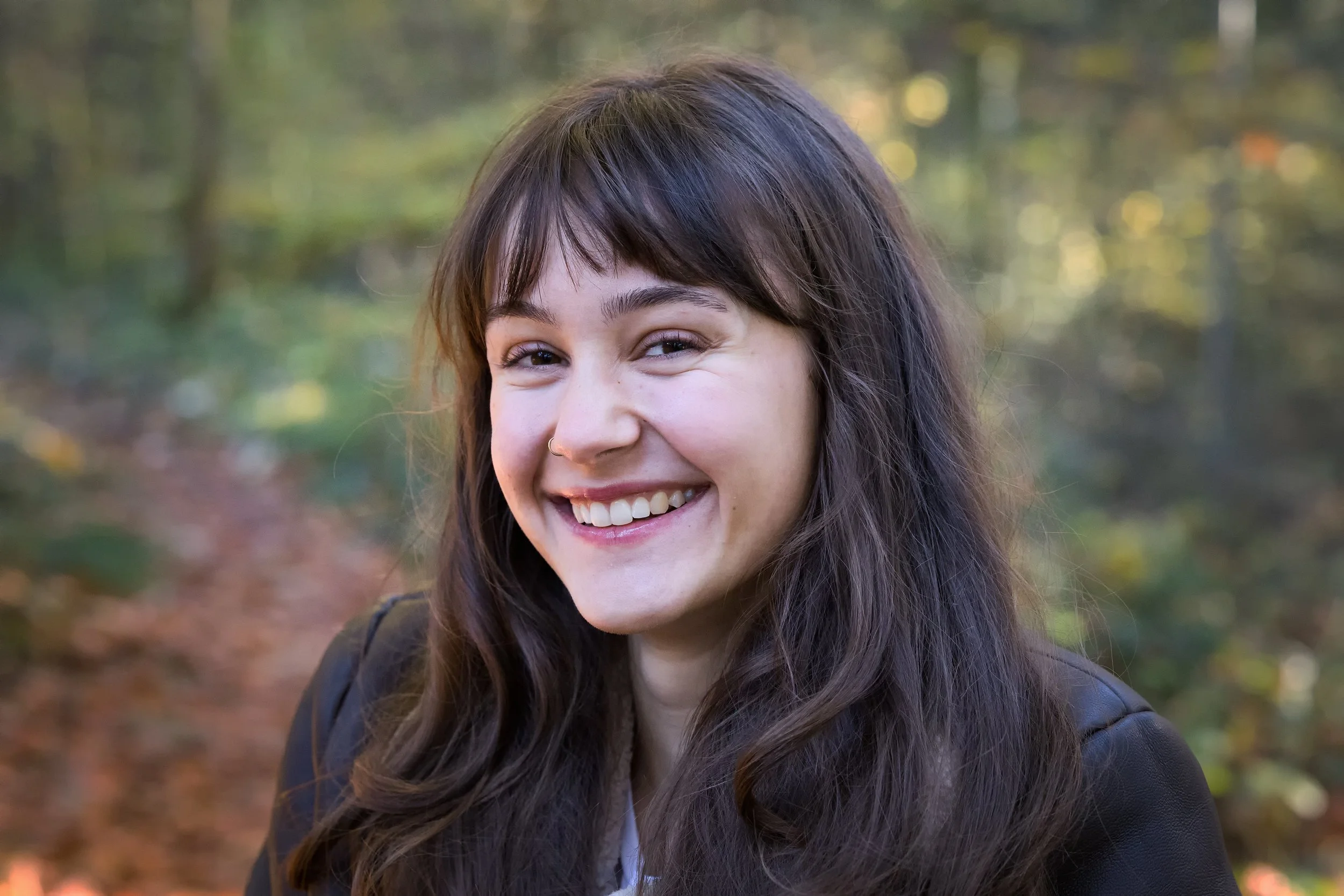 Ein junges Mädchen mit braunen Haaren, das im Wald lächelt.