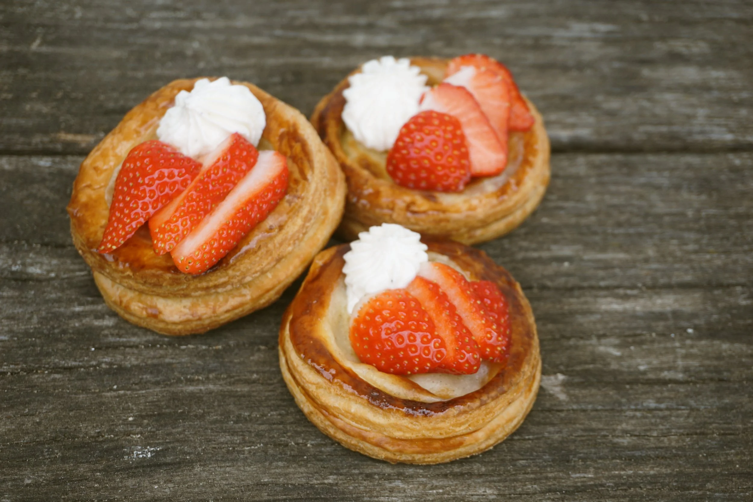 Runde Plunderteilchen mit Erdbeeren und Sahne auf einem Holztisch