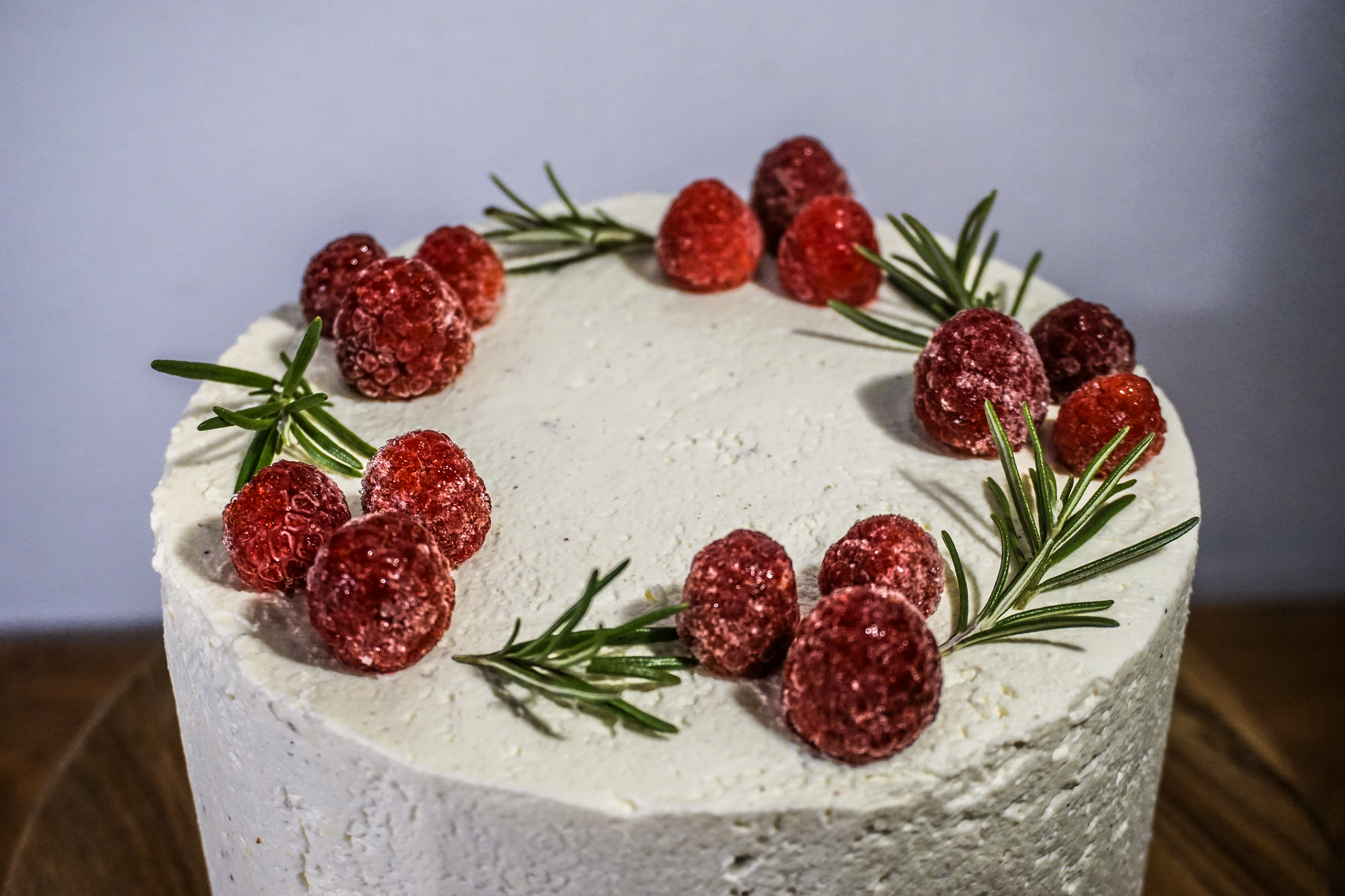 Eine weiße Torte mit Himbeeren und Rosmarinzweigen auf der Oberseite.
