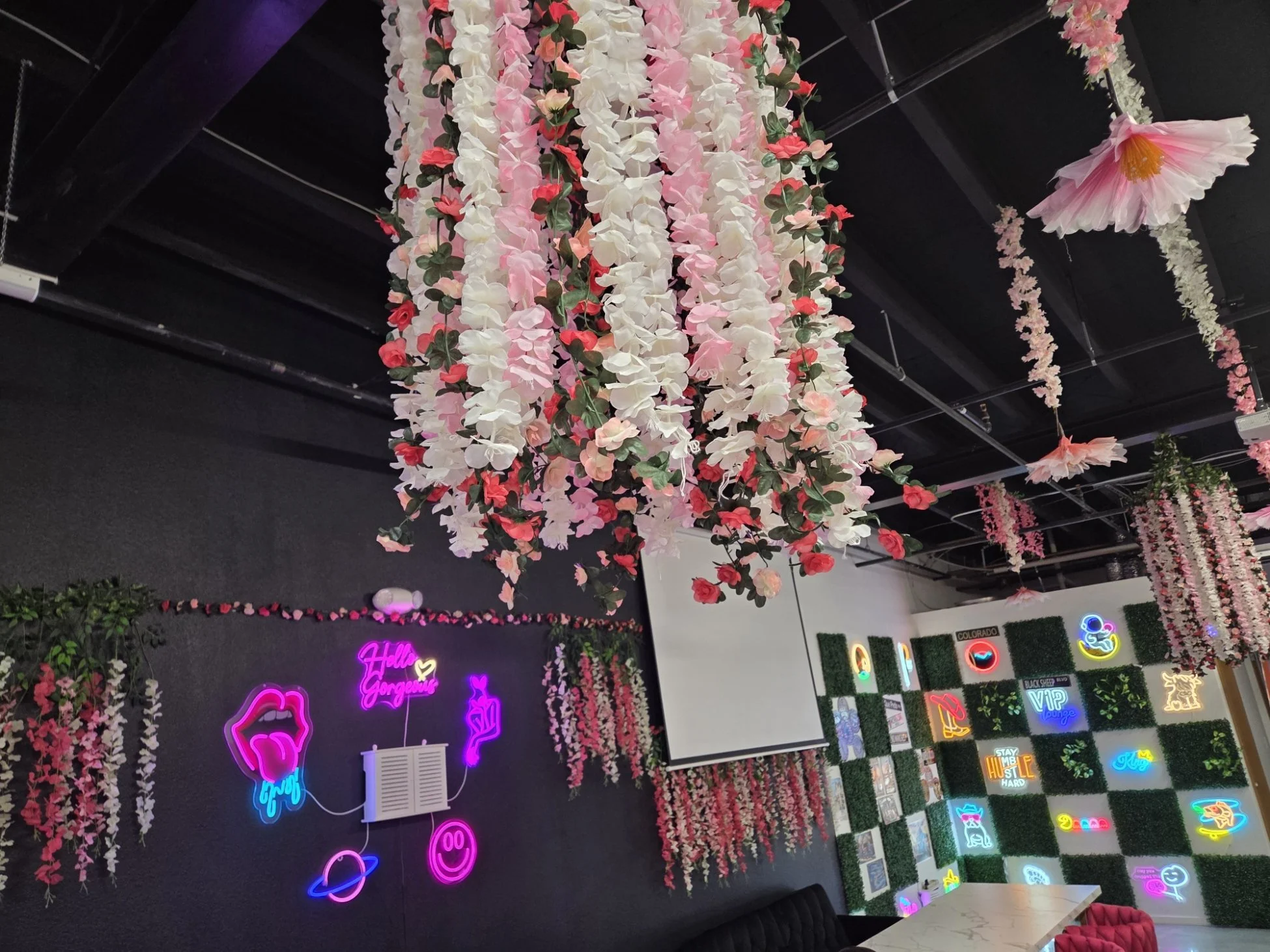Decorative hanging pink and white flowers with neon signs and wall art in a vibrant indoor space.
