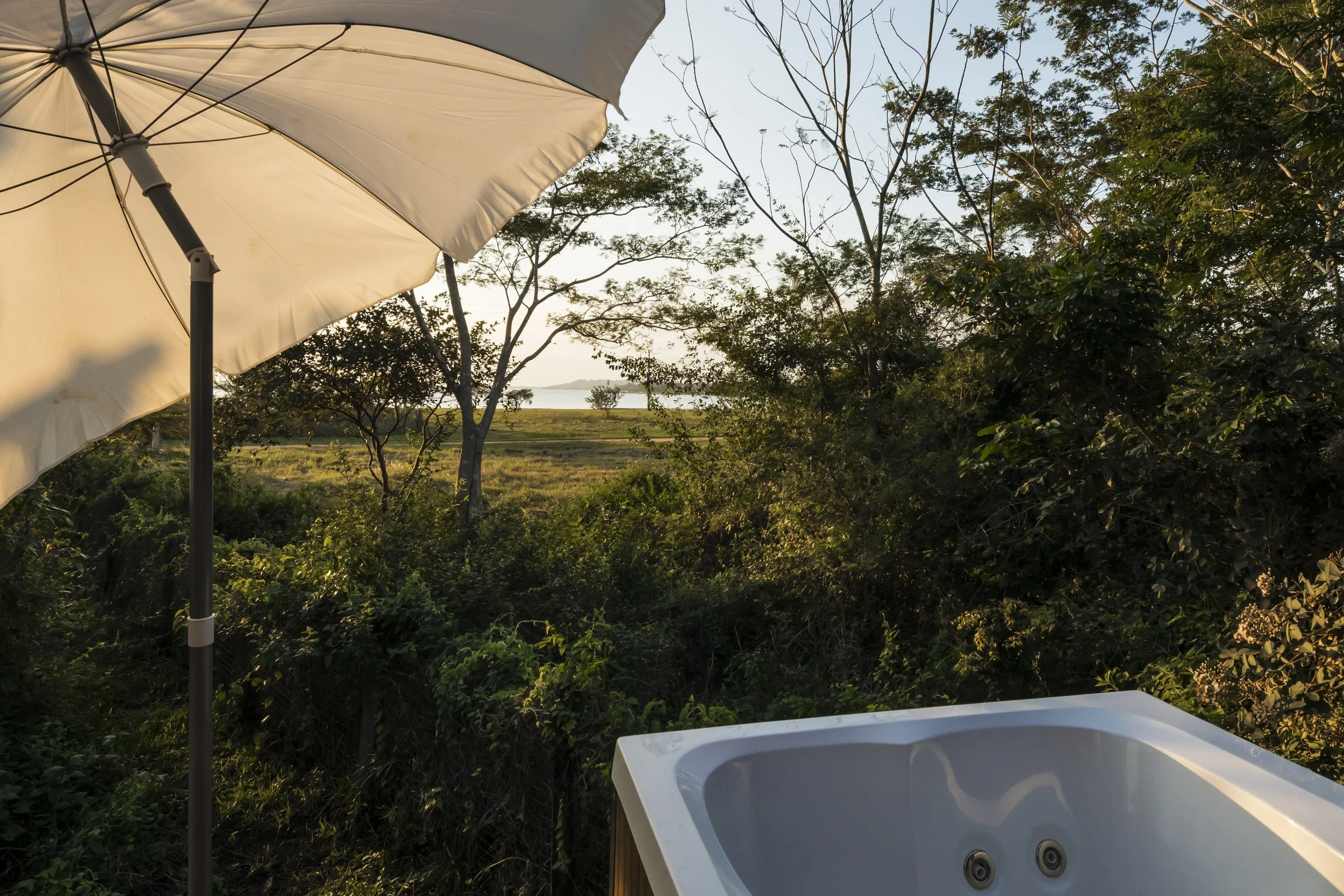PRO ARQUITECTURA PARAGUAY architecture design PROSA
Jacuzzi al aire libre con vista a la naturaleza, rodeado de árboles, con sombrilla blanca y un paisaje hacia un lago o río en el horizonte, durante el atardecer.