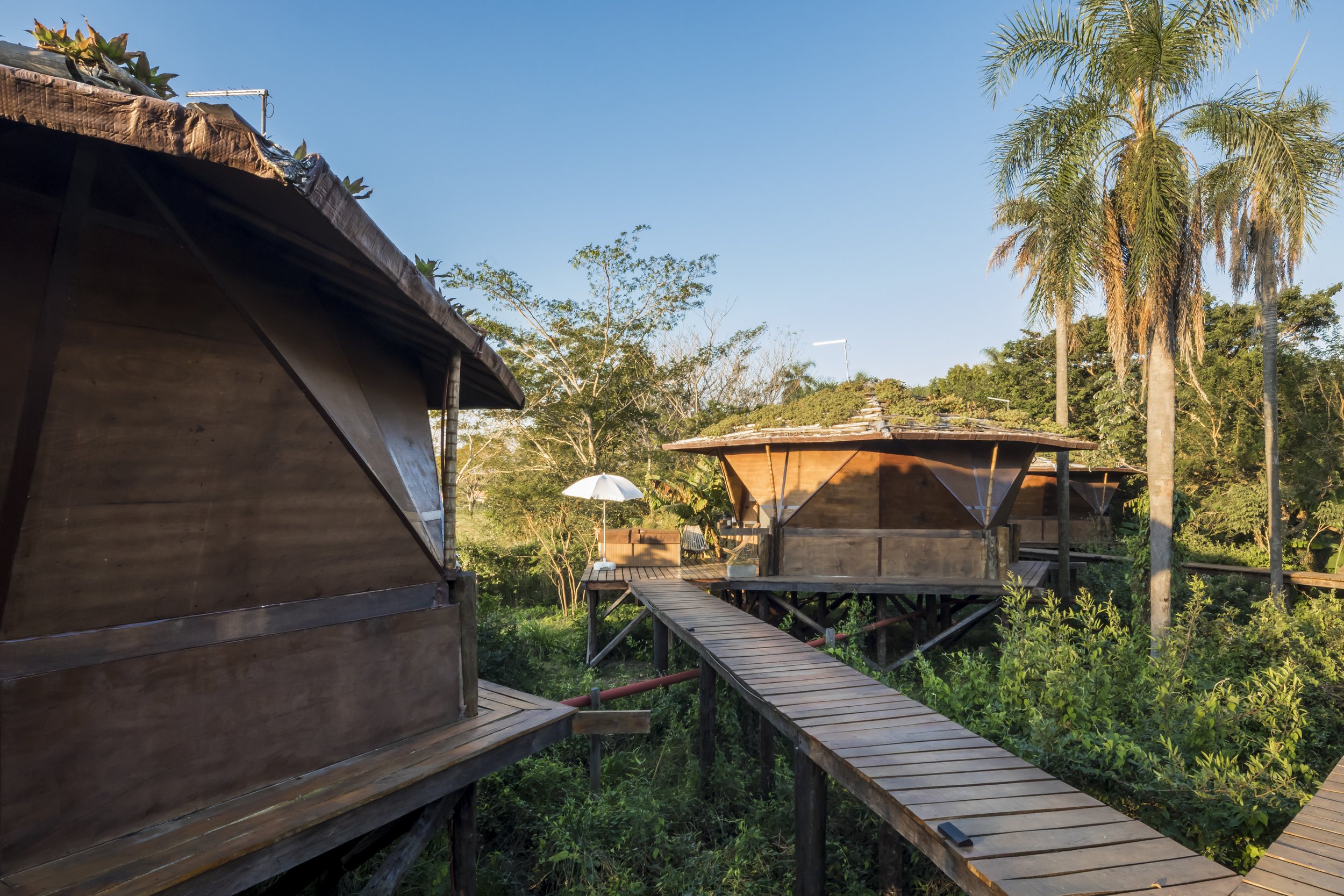 PRO ARQUITECTURA PARAGUAY architecture design PROSA
Casas de madera en un entorno natural con árboles y un camino de madera elevado