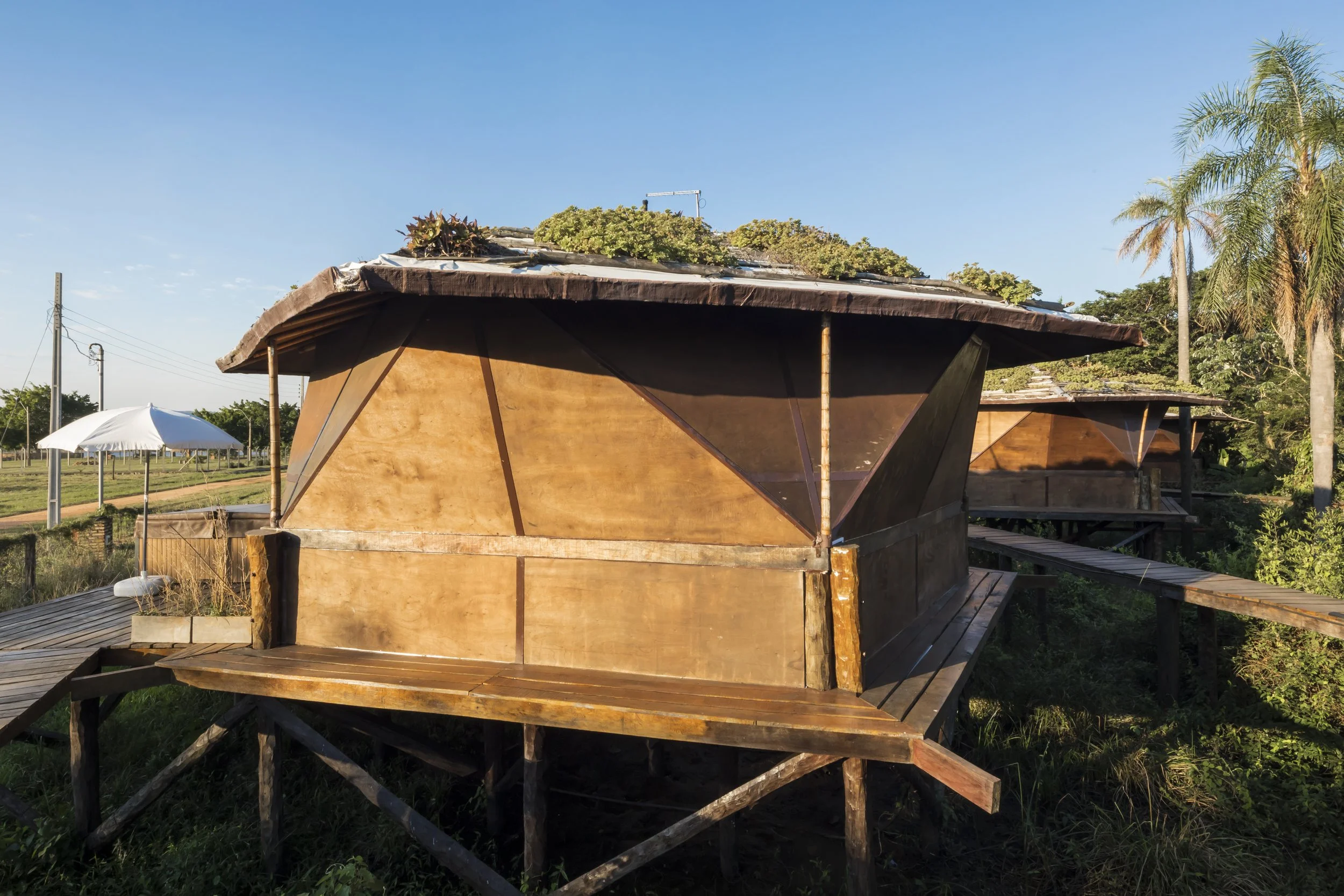 PRO ARQUITECTURA PARAGUAY architecture design PROSA
Casa de madera sobre pilotes en un entorno natural con árboles y césped, bajo un cielo azul.