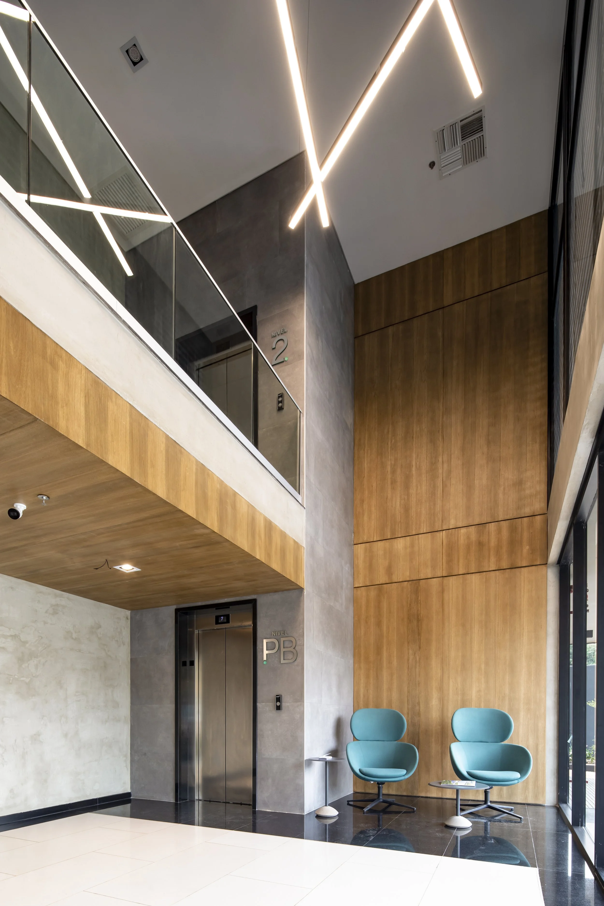 PRO ARQUITECTURA PARAGUAY architecture design PROSA
Vestíbulo moderno con paredes de madera, con elevadores y sillas azules.