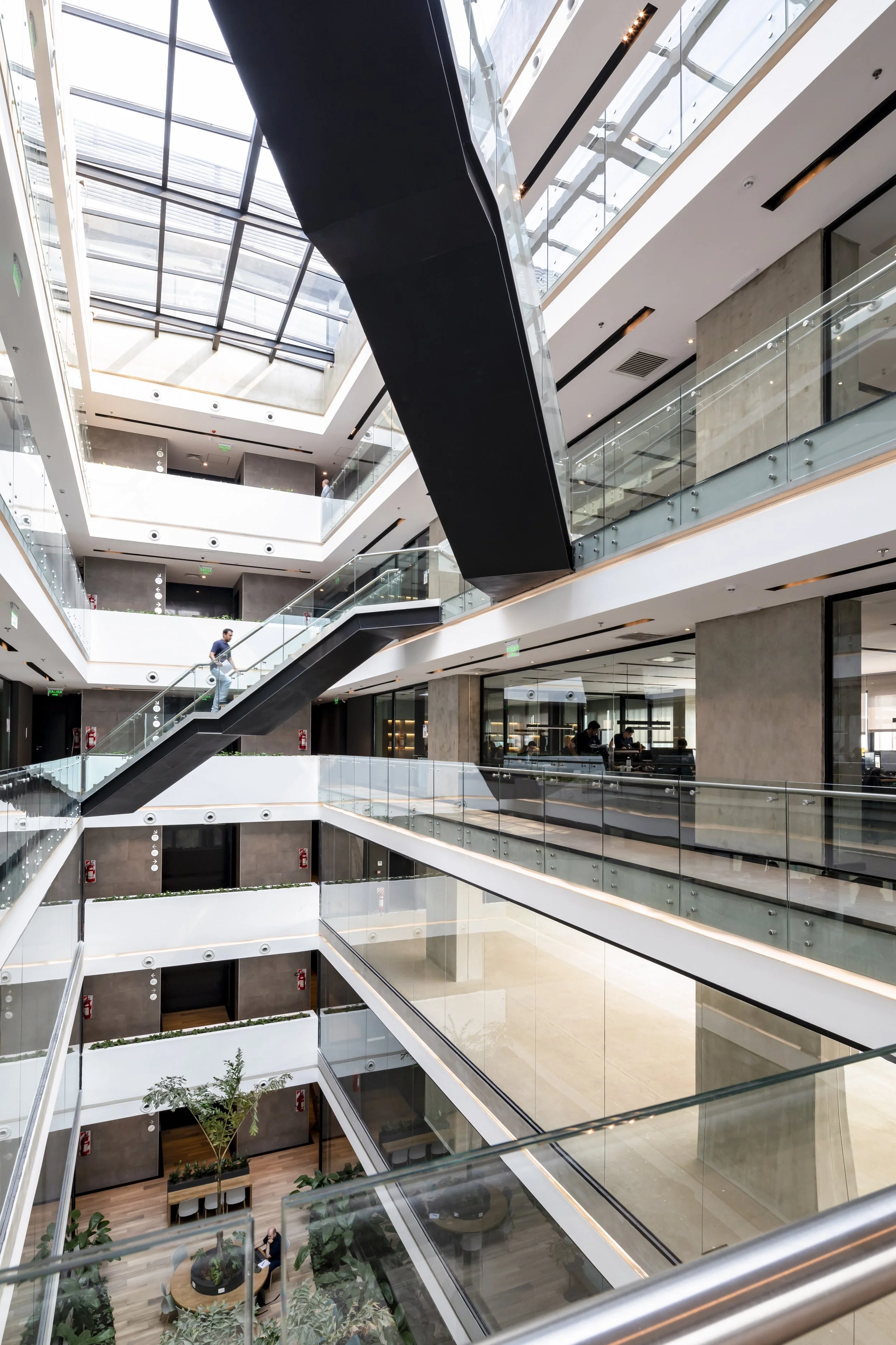 PRO ARQUITECTURA PARAGUAY architecture design PROSA
Interior de un edificio moderno con varias plantas y escaleras de vidrio y metal, con luz natural entrando por un tragaluz en el techo.