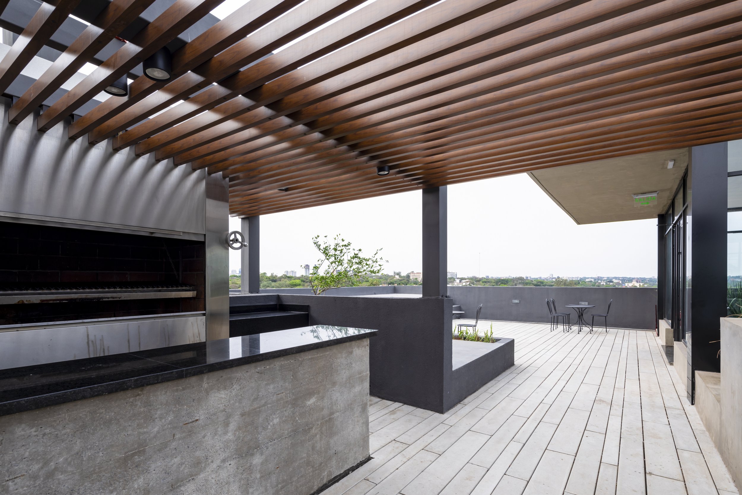PRO ARQUITECTURA PARAGUAY architecture design PROSA
Terraza con barbacoa, suelo de madera y mobiliario de metal, vista panorámica de la ciudad.