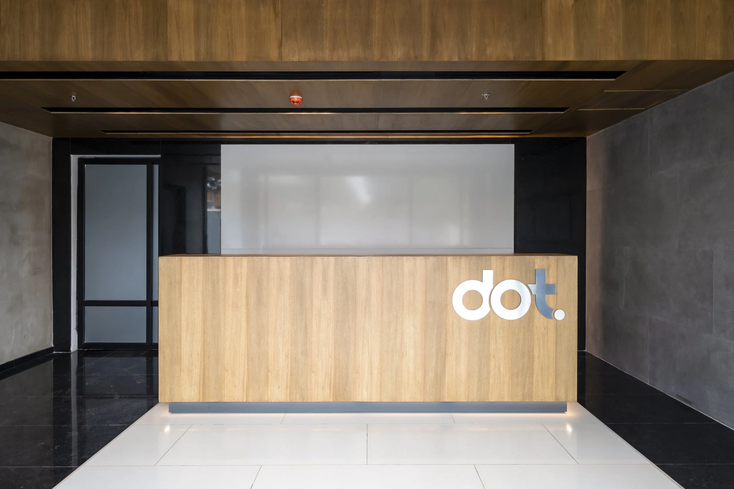 PRO ARQUITECTURA PARAGUAY architecture design PROSA
Mostrador de recepción en una oficina con el logotipo 'dot' en letras blancas y azul, entorno moderno con paredes de madera y pisos de cerámica negra y blanca