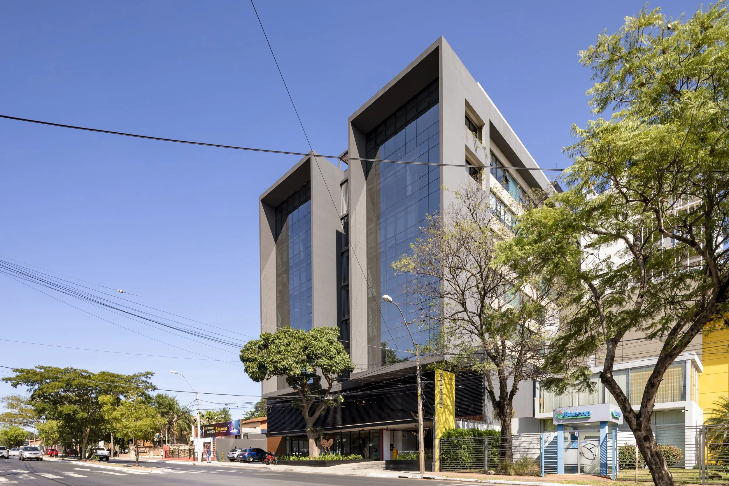 PRO ARQUITECTURA PARAGUAY architecture design PROSA
Edificio moderno de varios pisos con fachada de ventanas de cristal, árboles en la calle y cielo despejado.