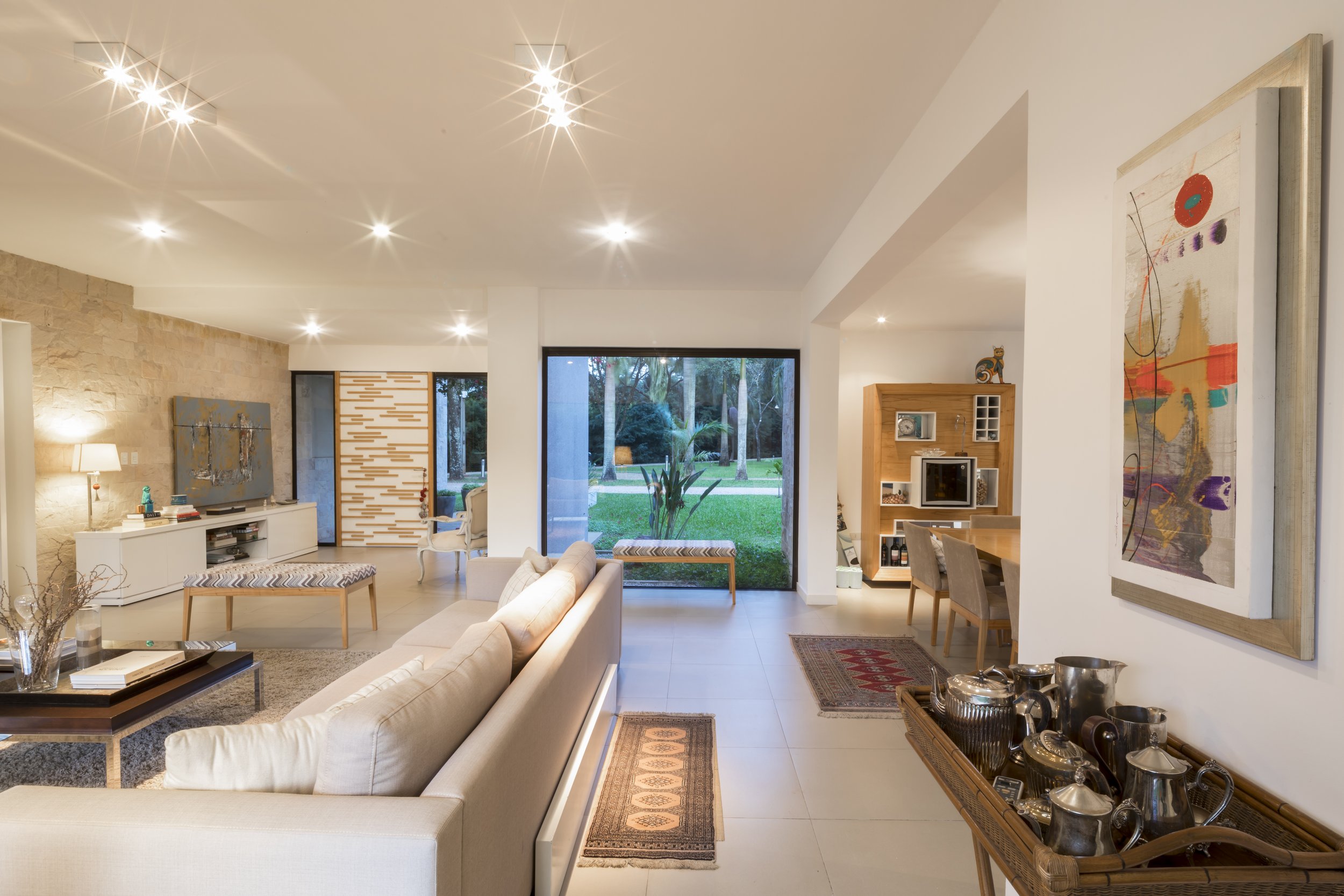 PRO ARQUITECTURA PARAGUAY architecture design PROSA
Sala de estilo moderno con sofá beige, mesa de centro y alfombra, paredes blancas, ventanas grandes con vista a jardín con árboles, decoración con cuadros y muebles de madera.