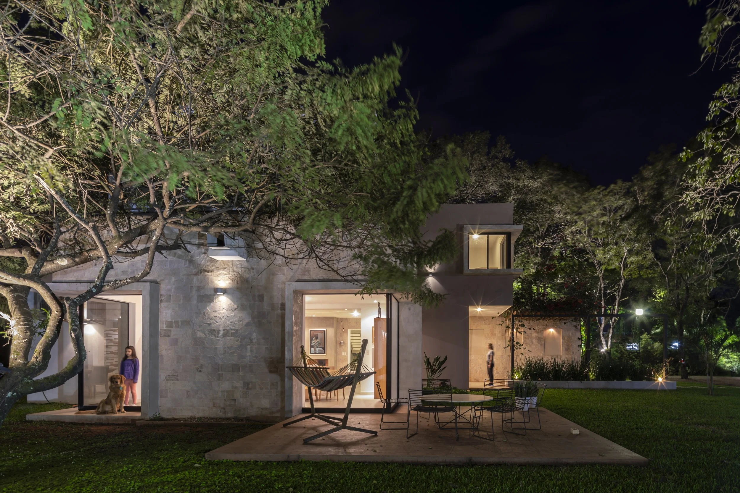 Casa moderna iluminada en la noche con patio y árboles