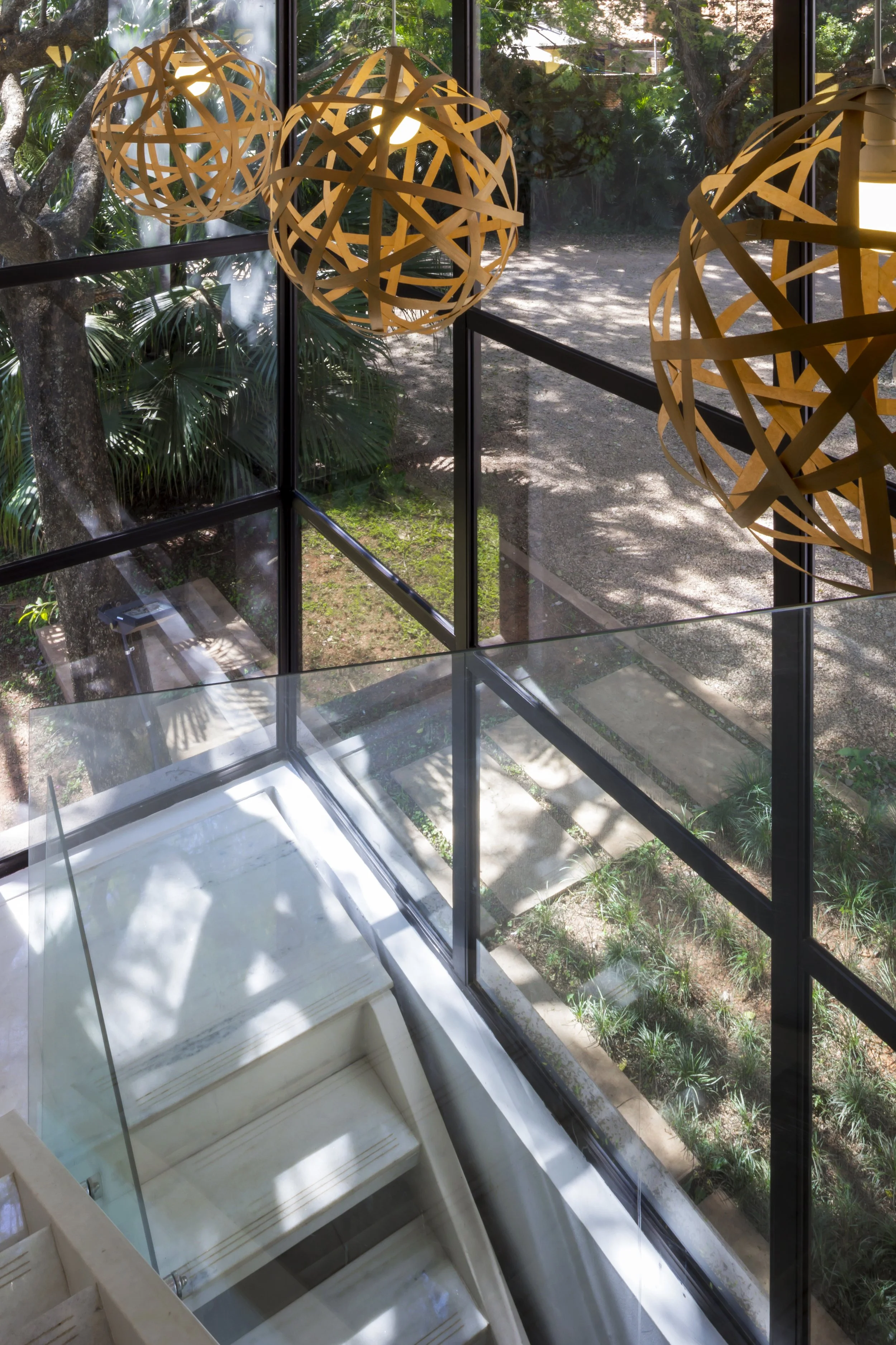 Lámparas esféricas de diseño moderno colgando del techo junto a ventanas grandes con vista a un jardín con árboles y plantas.