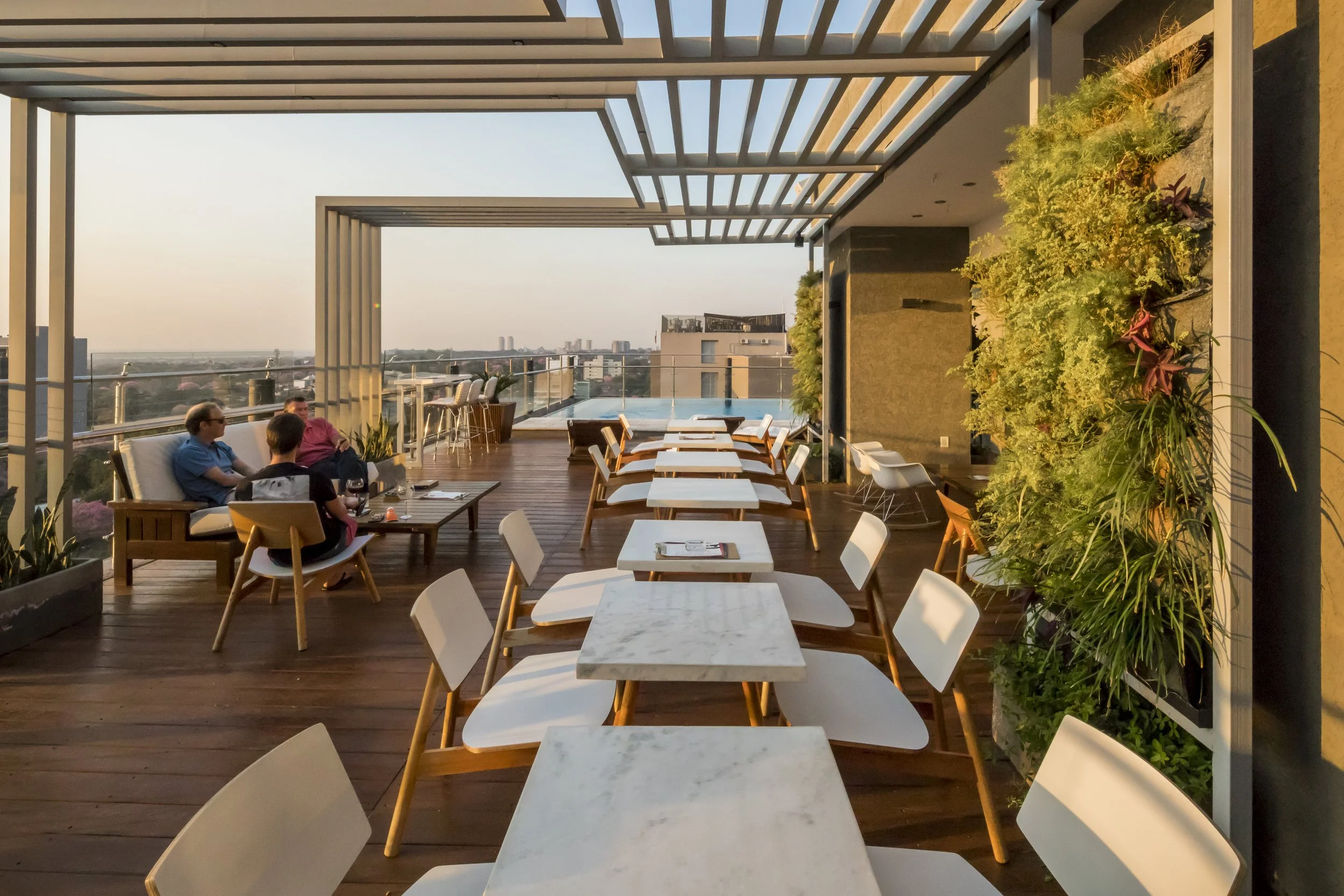 Terraza del restaurante con mesas y sillas, vista panorámica de la ciudad, plantas decorativas.